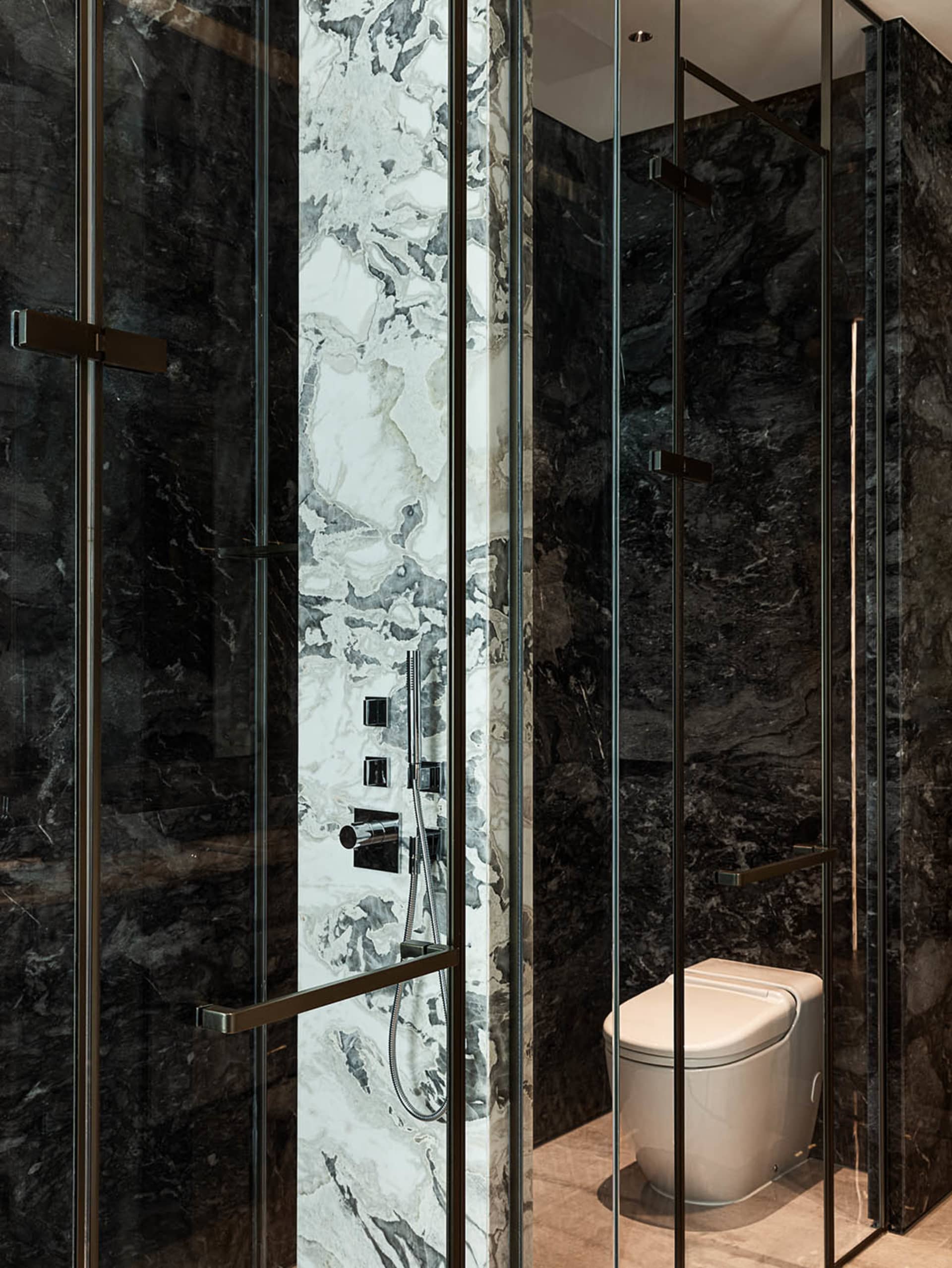 Modern bathroom with dark marble walls and glass shower enclosure.