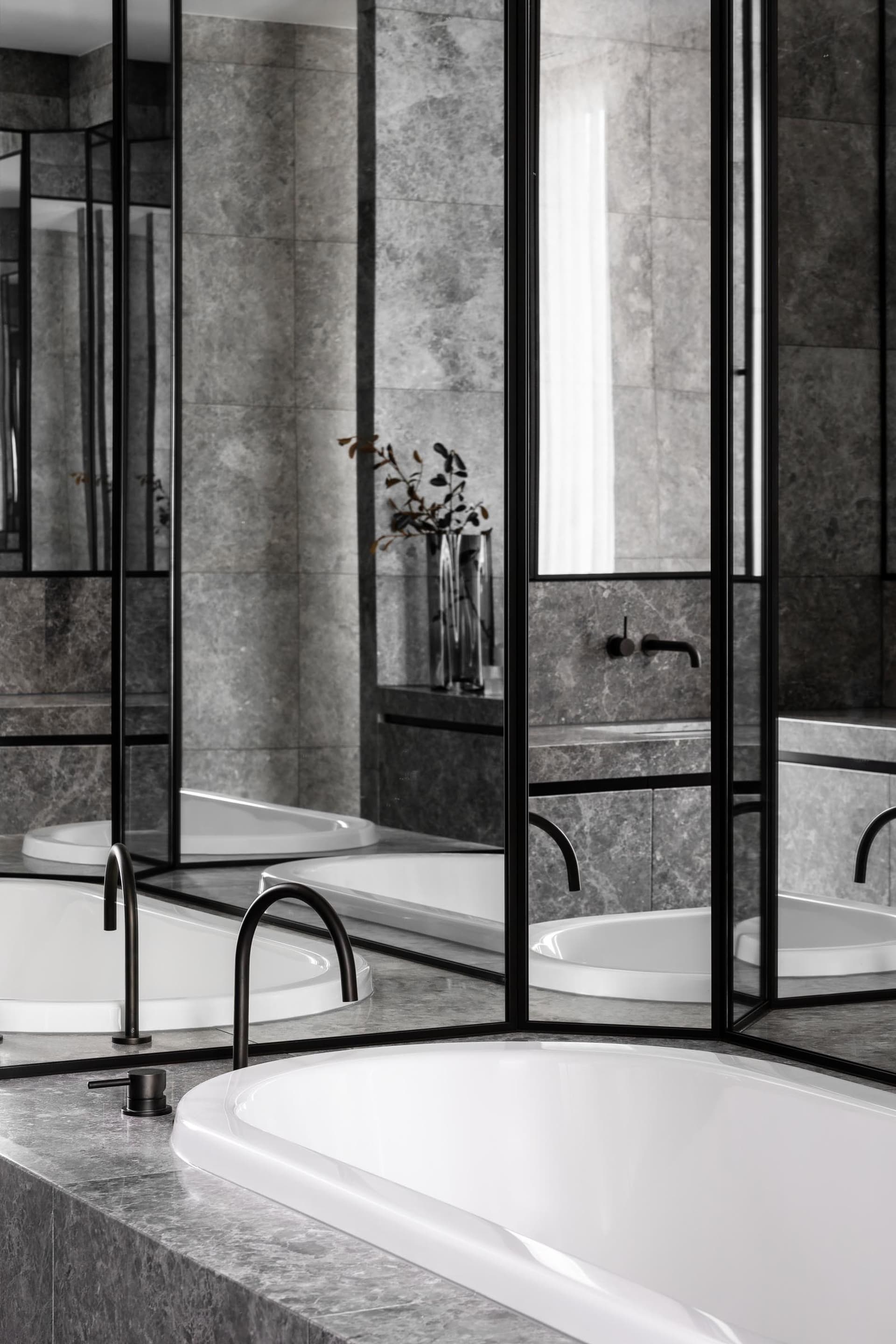 Modern, minimalist bathroom featuring grey marble tiles and a sleek white bathtub.