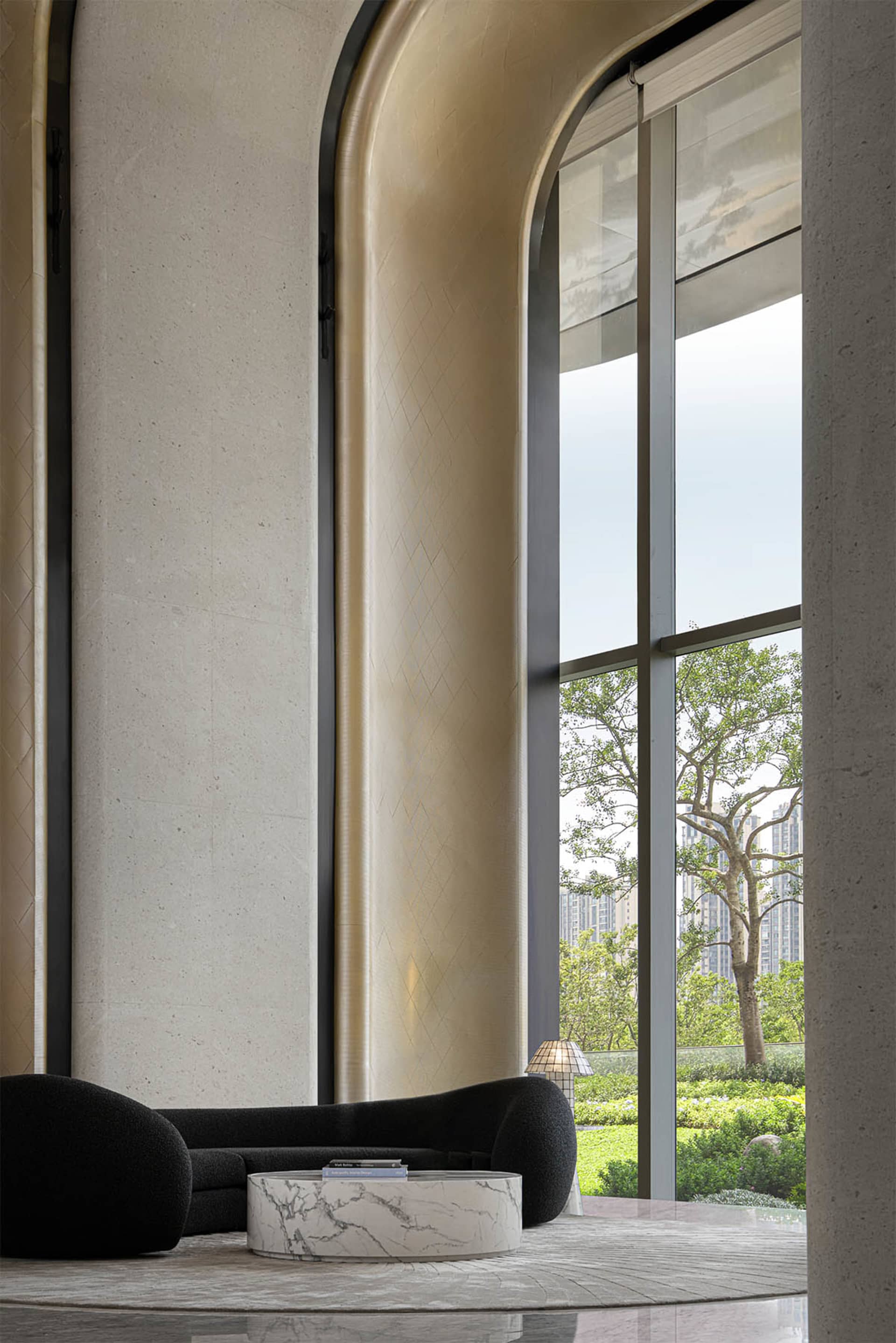 Modern lobby interior with large glass windows displaying outdoor greenery and a sleek, minimalist seating area with marble c