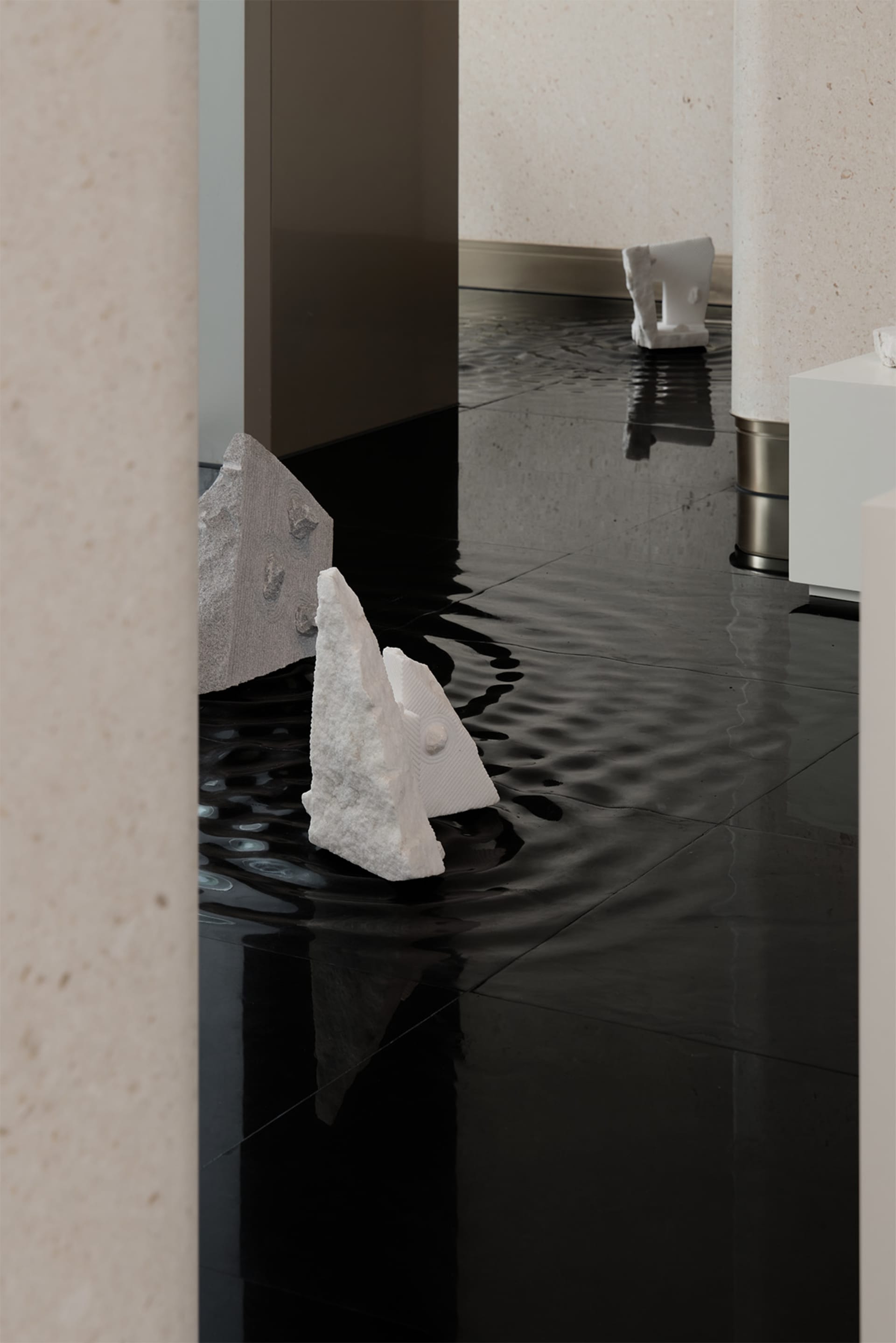 Modern marble interior art installation featuring water flooding on glossy black floor tiles.