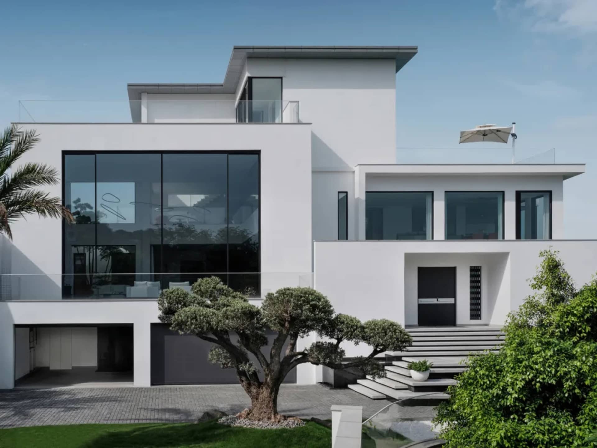 Modern house exterior with large glass windows, white walls, and a minimalist design.