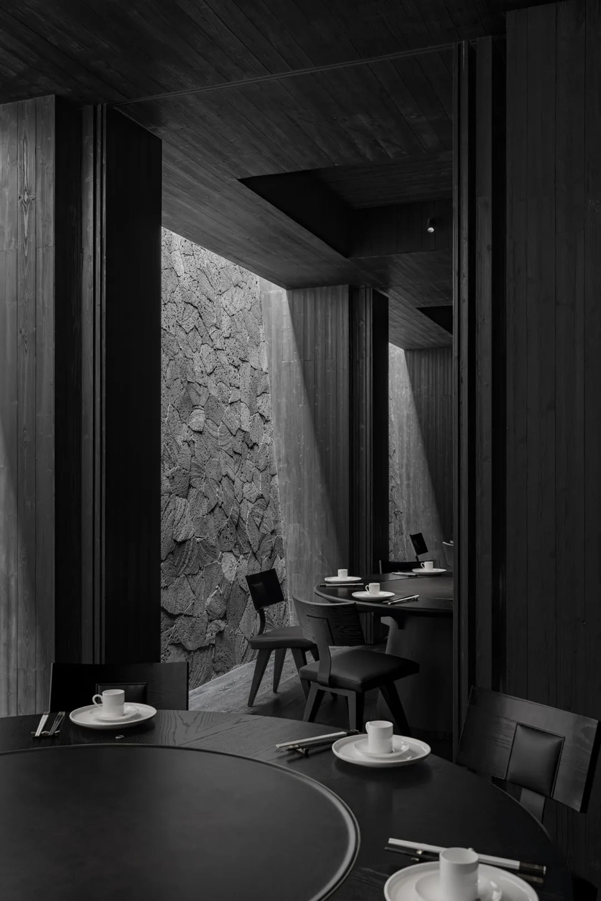 A modern minimalist restaurant interior with dark wooden and concrete materials.