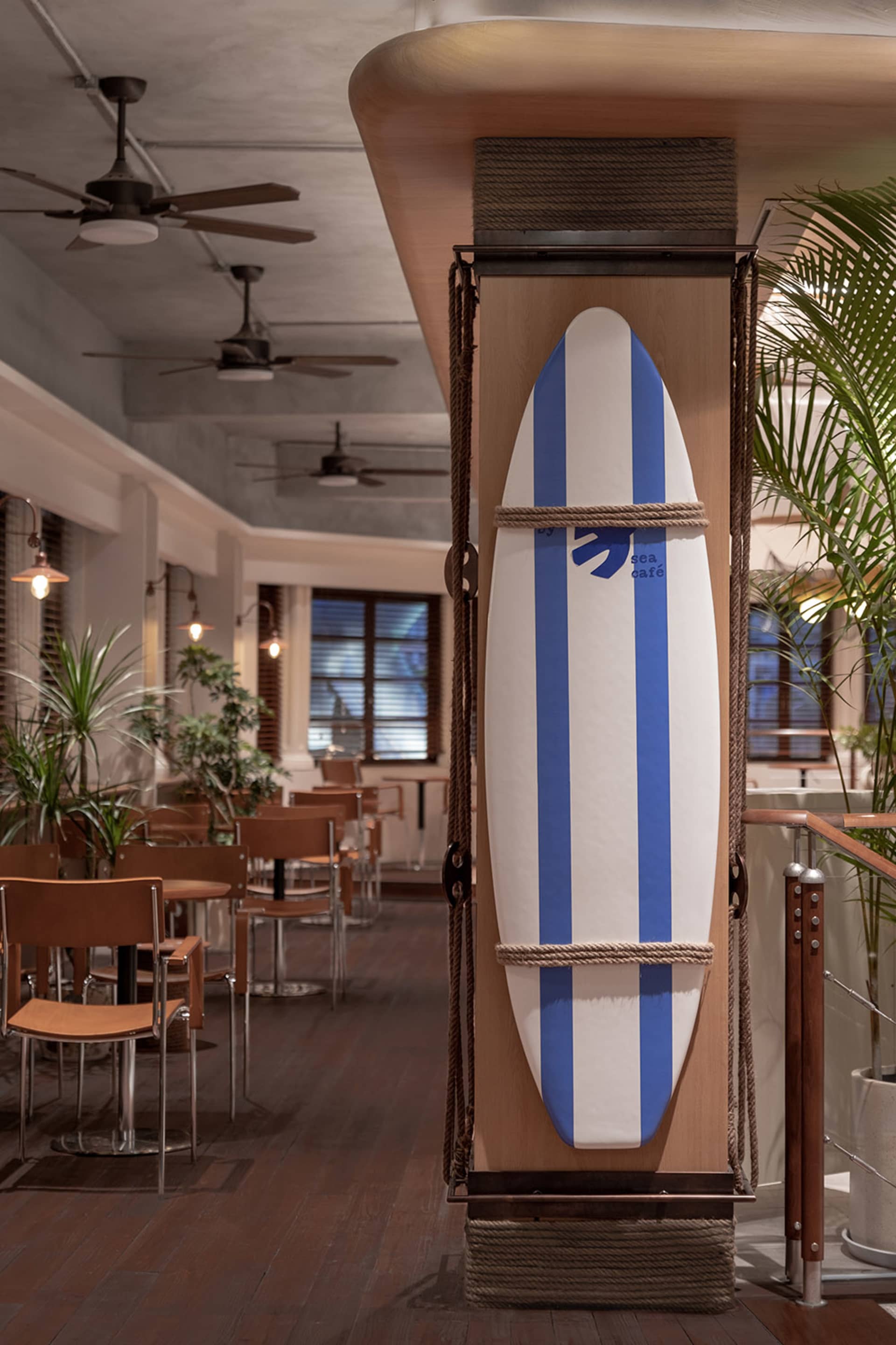 A surfboard decorated with blue stripes and the logo 'Sea Cafe' is mounted in a coastal-themed restaurant interior with woode