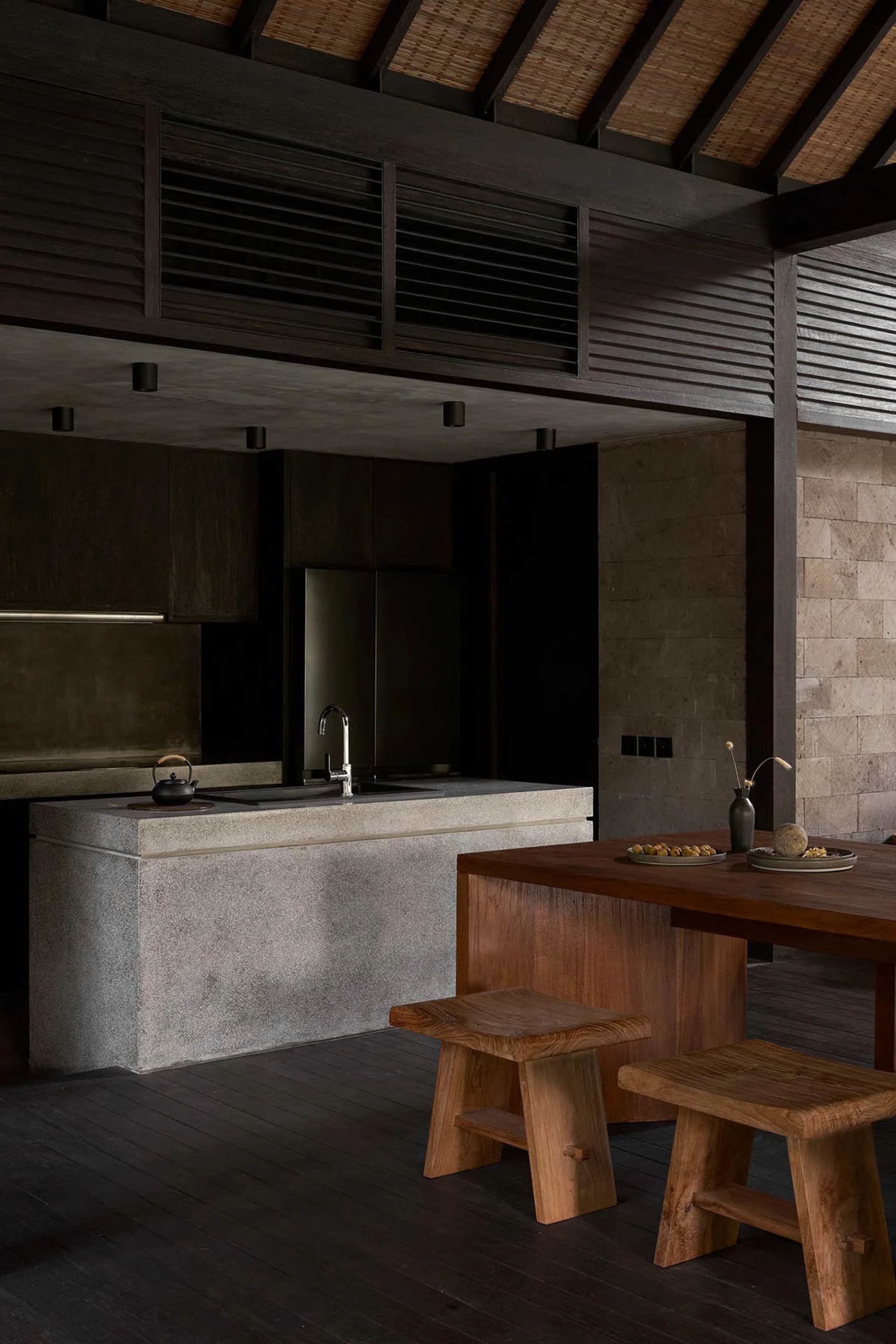 A modern kitchen with a concrete countertop, wooden stools, and a minimalist design.