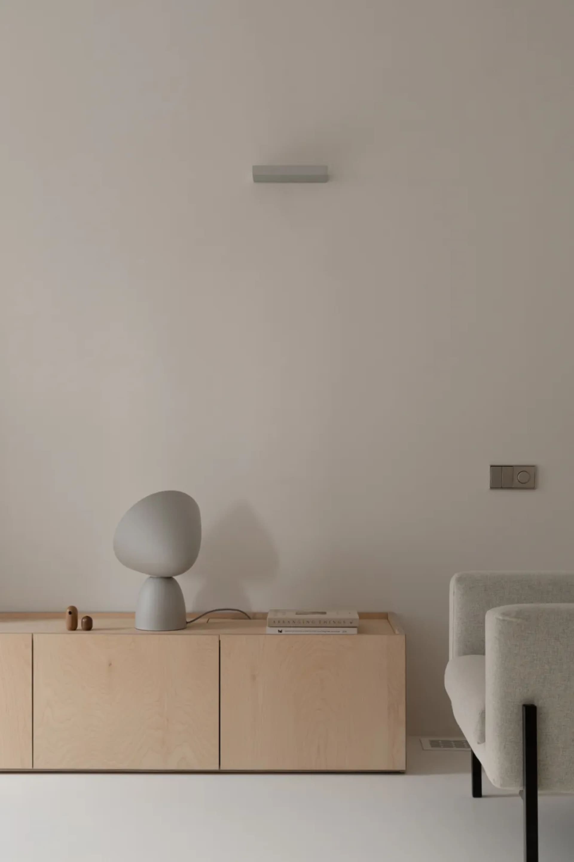 A minimalist living space featuring a sleek, light-colored cabinet with a unique, grey table lamp and a white armchair.