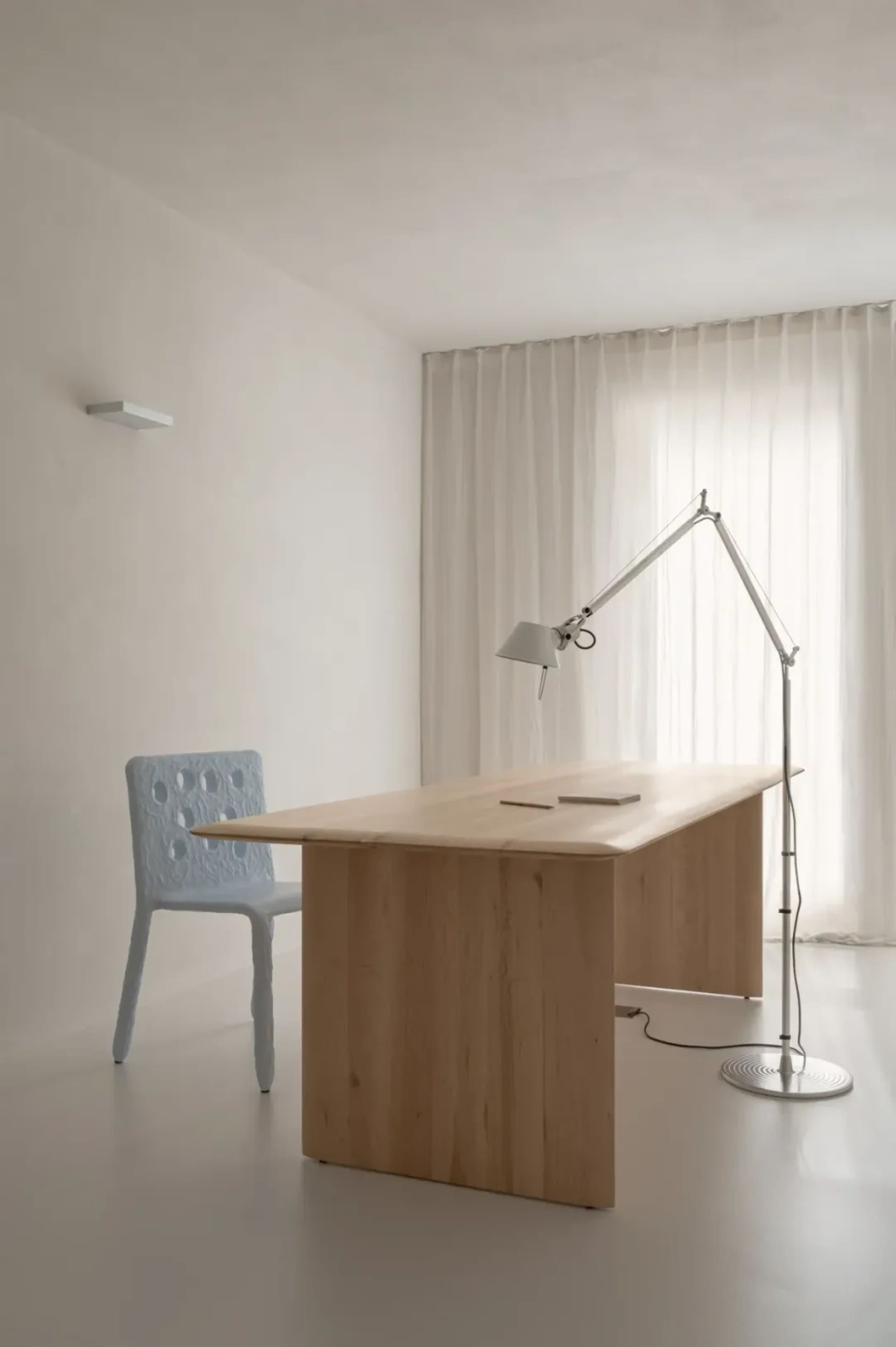A minimalist home office featuring a wooden desk and blue woven chair with a floor lamp