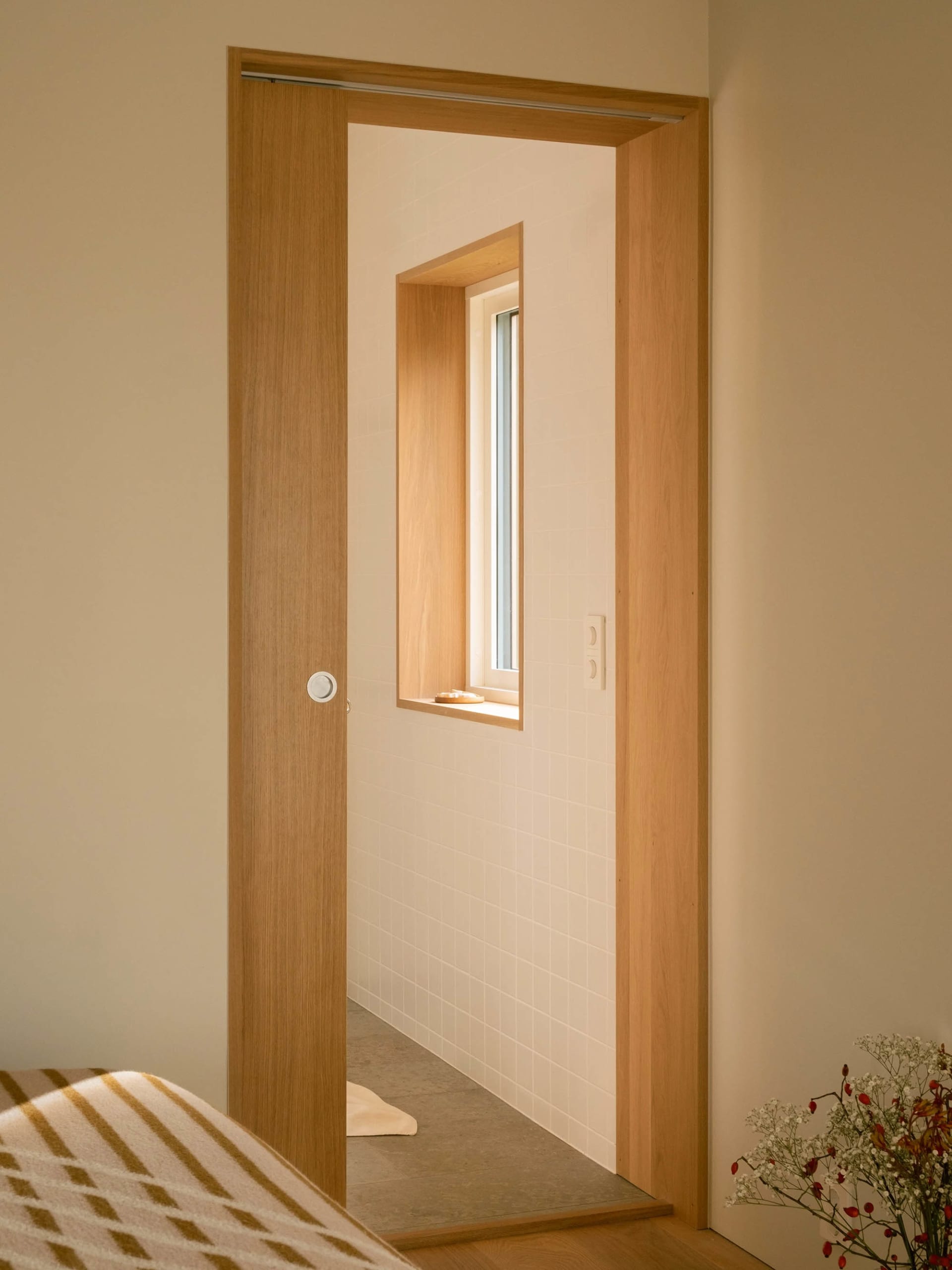 Modern minimalist bathroom with white walls, a wood door, and a small window.