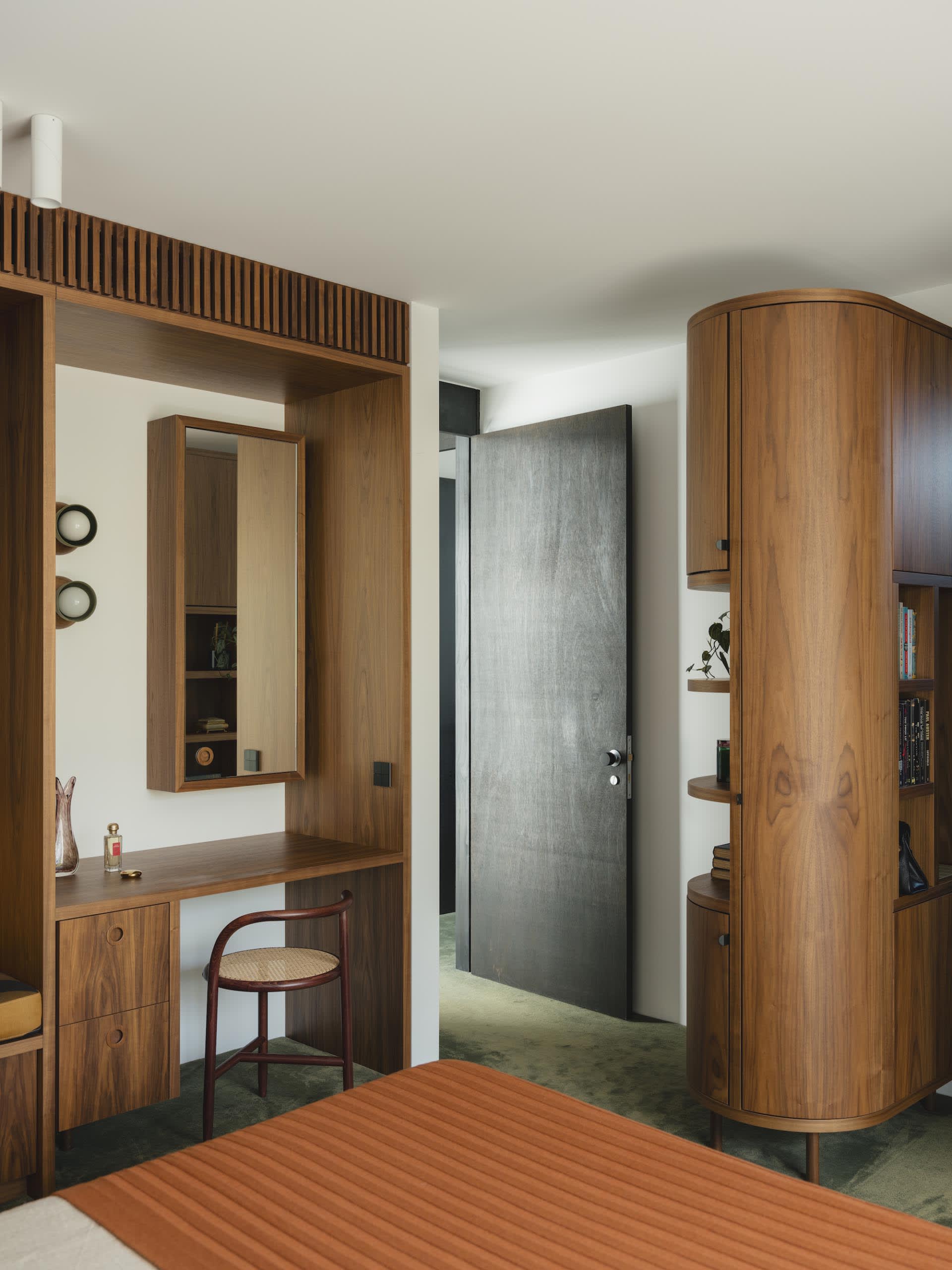 A modern bedroom with wooden furniture including a bed with a striped covering, a vanity with a mirror and a wooden chair.