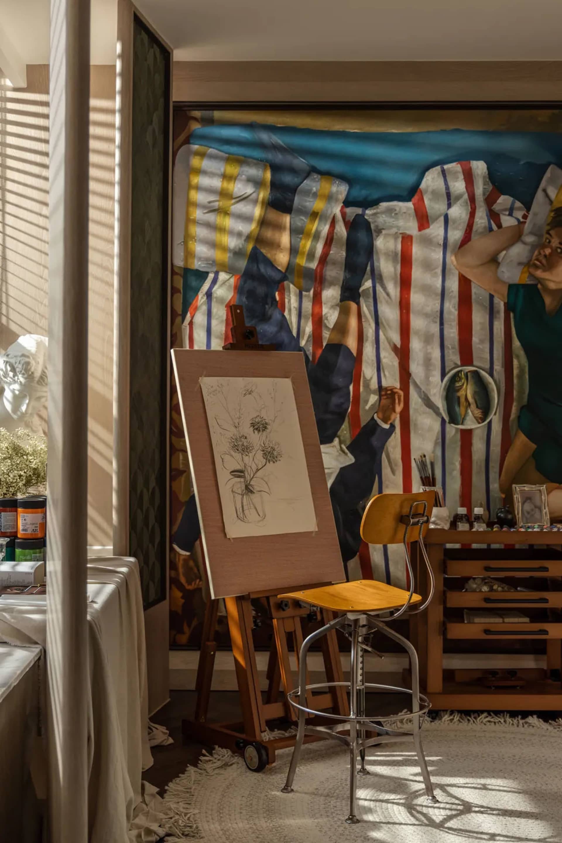 An artist studio with a large mural, easel, and sketch on a canvas.