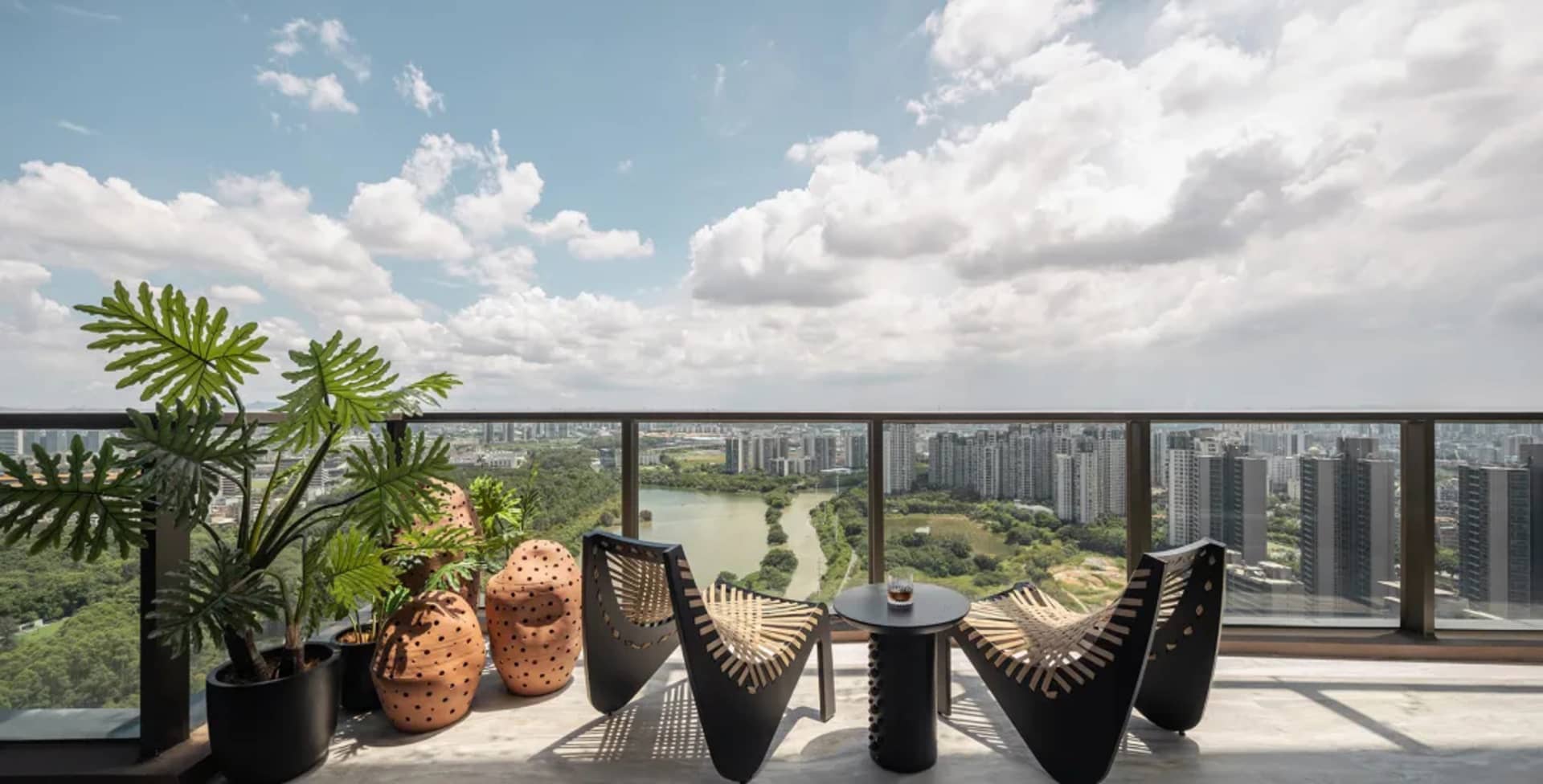 A modern balcony featuring concrete furniture, plants in pots, and a view of a cityscape.