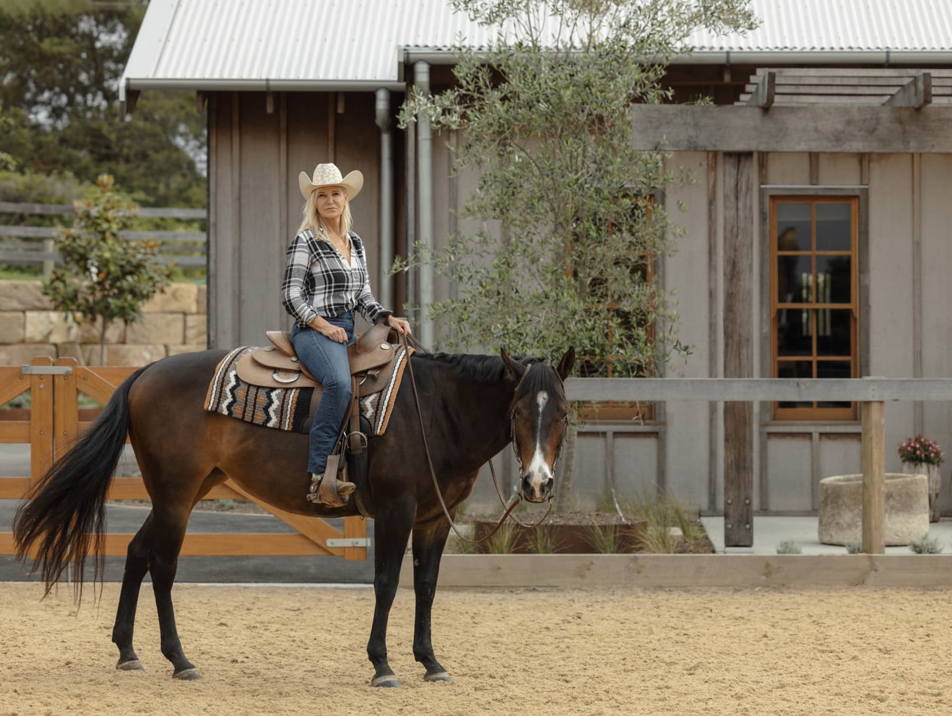 A woman rides a horse in a wooden-styled farm setting.