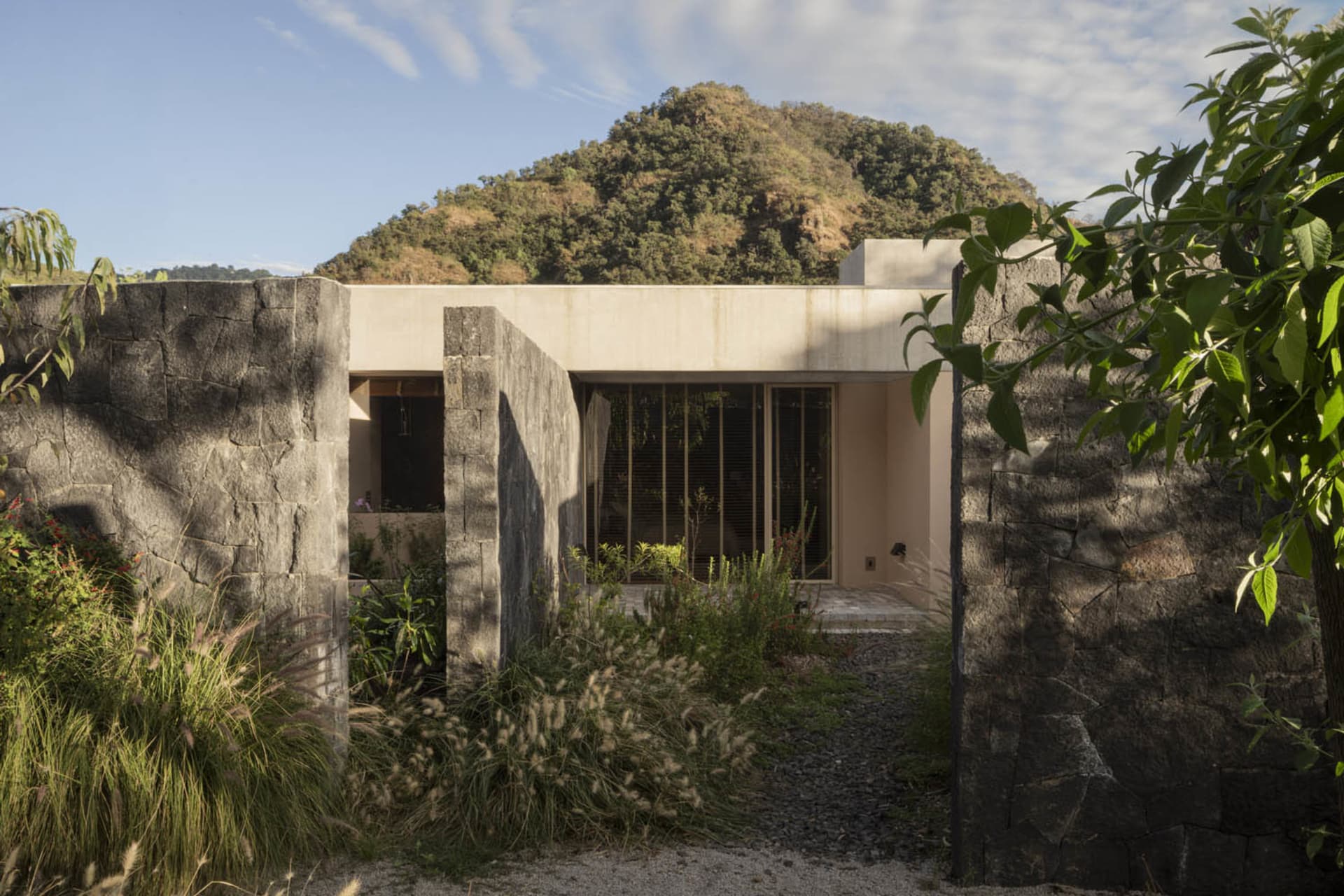 A modernist house with concrete exterior and large windows, situated against a scenic mountain backdrop.