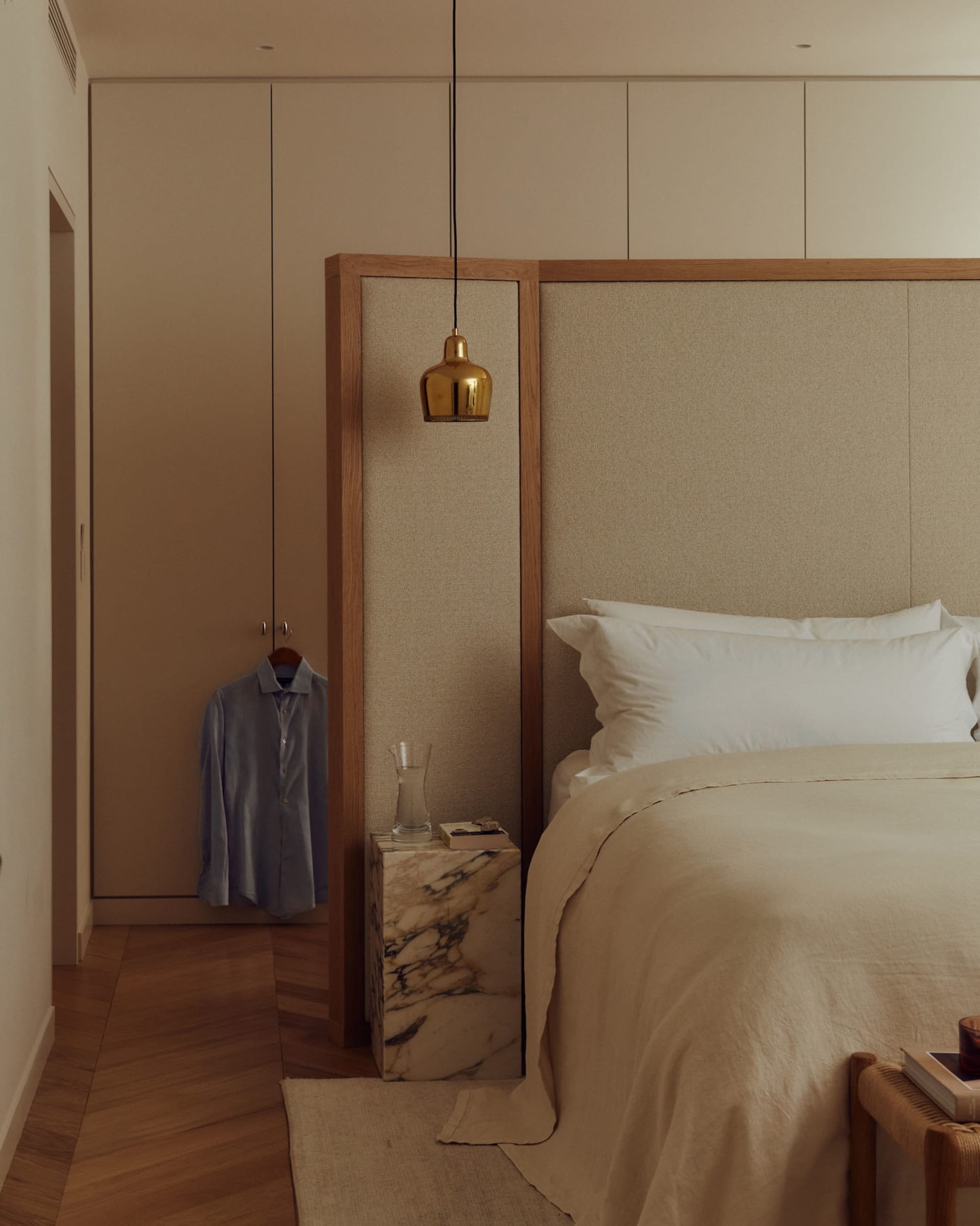 A modern bedroom featuring a fabric-covered bed and marble nightstand.
