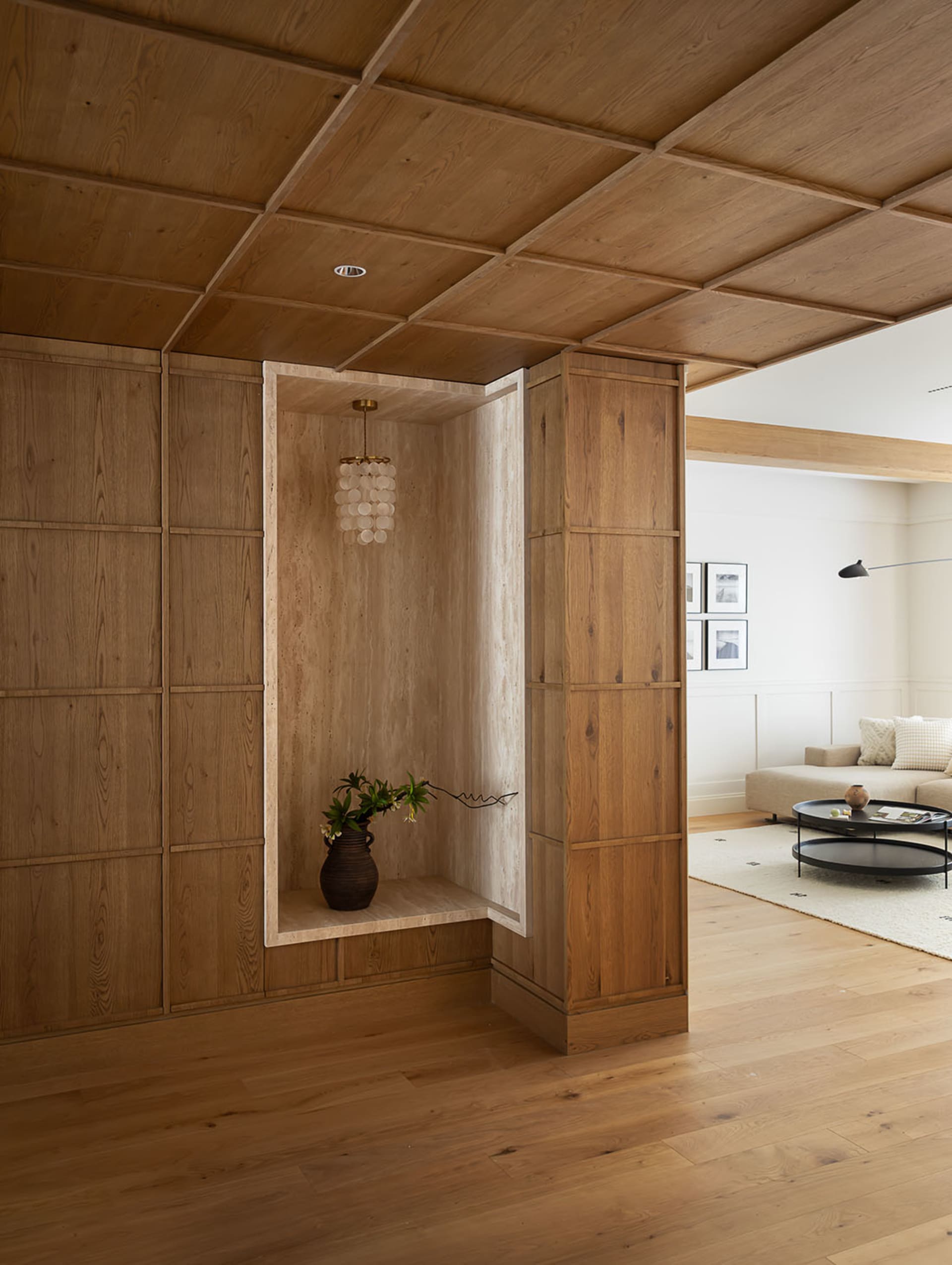 A modern living room with wood flooring and walls, featuring a cozy seating area and a decorative plant shelf.