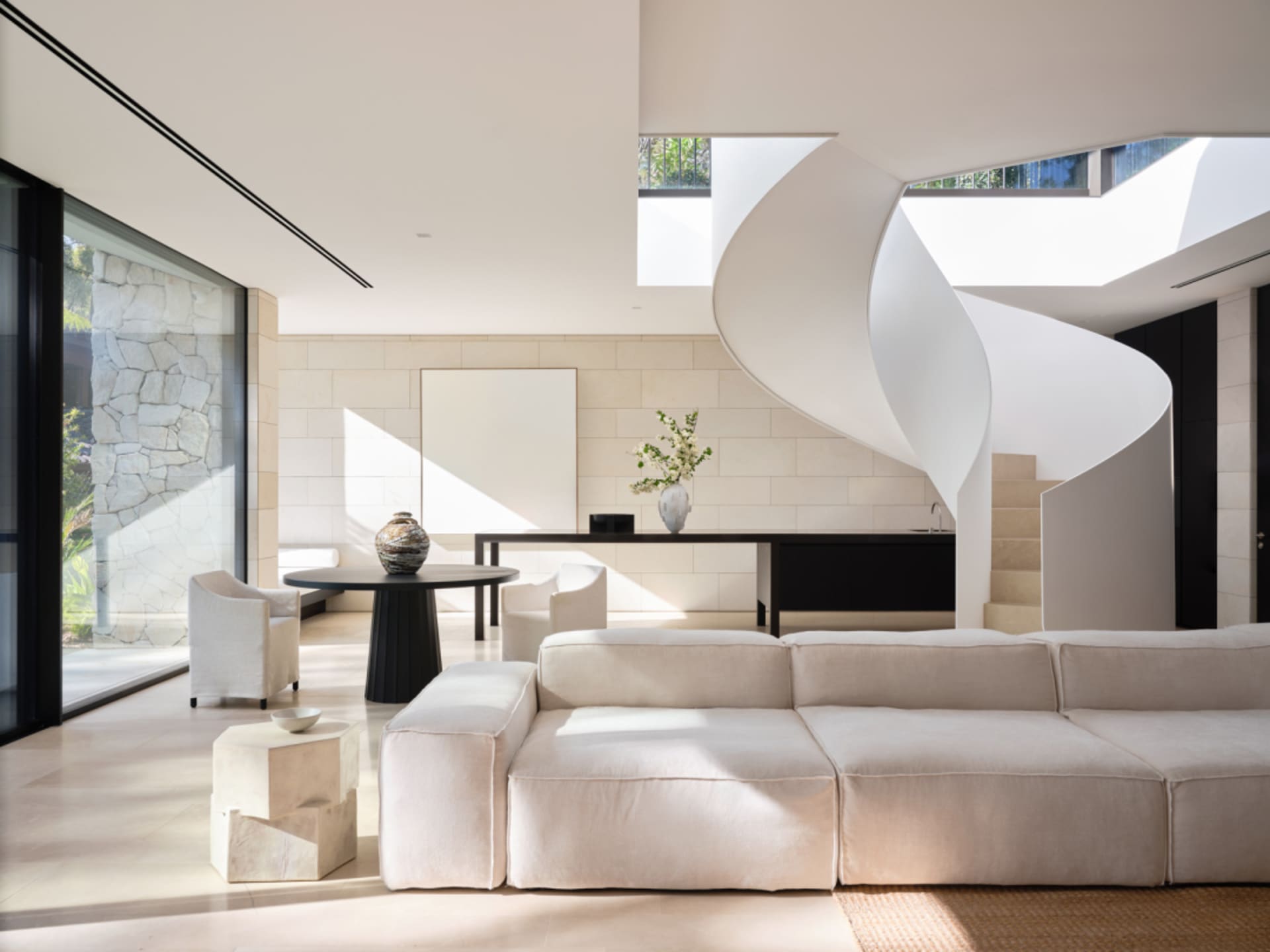 A modern living room with a concrete floor, white spiral staircase, large window, and minimalist furniture.