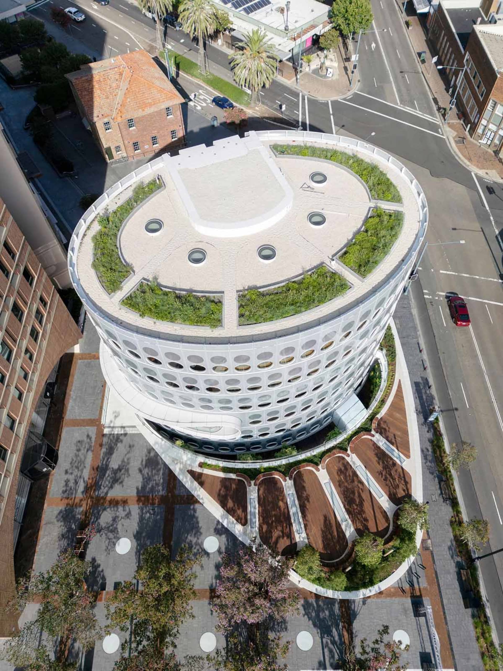 Aerial view of a modern building with a green roof surrounded by streets and trees.