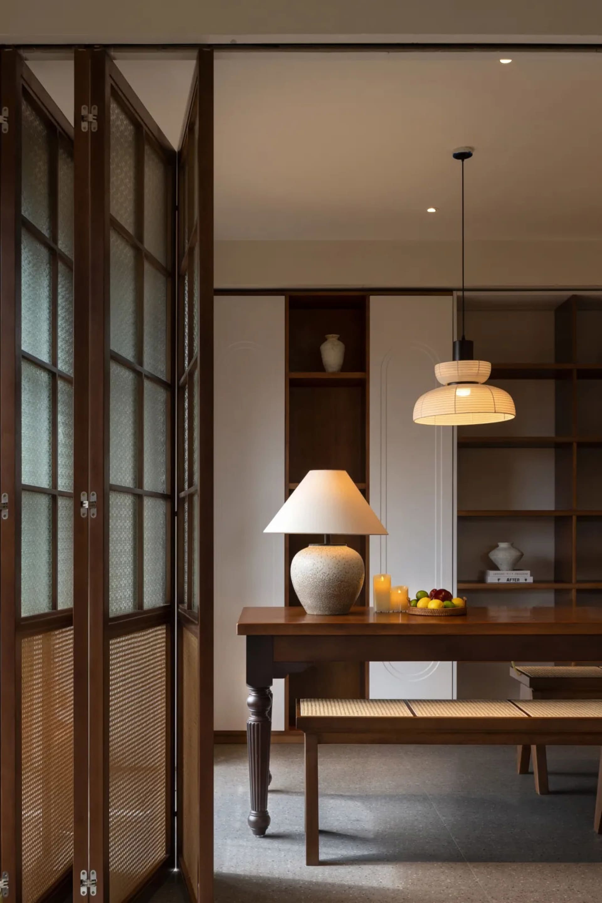 A modern dining room featuring wooden furniture, a table lamp, and a fruit basket.