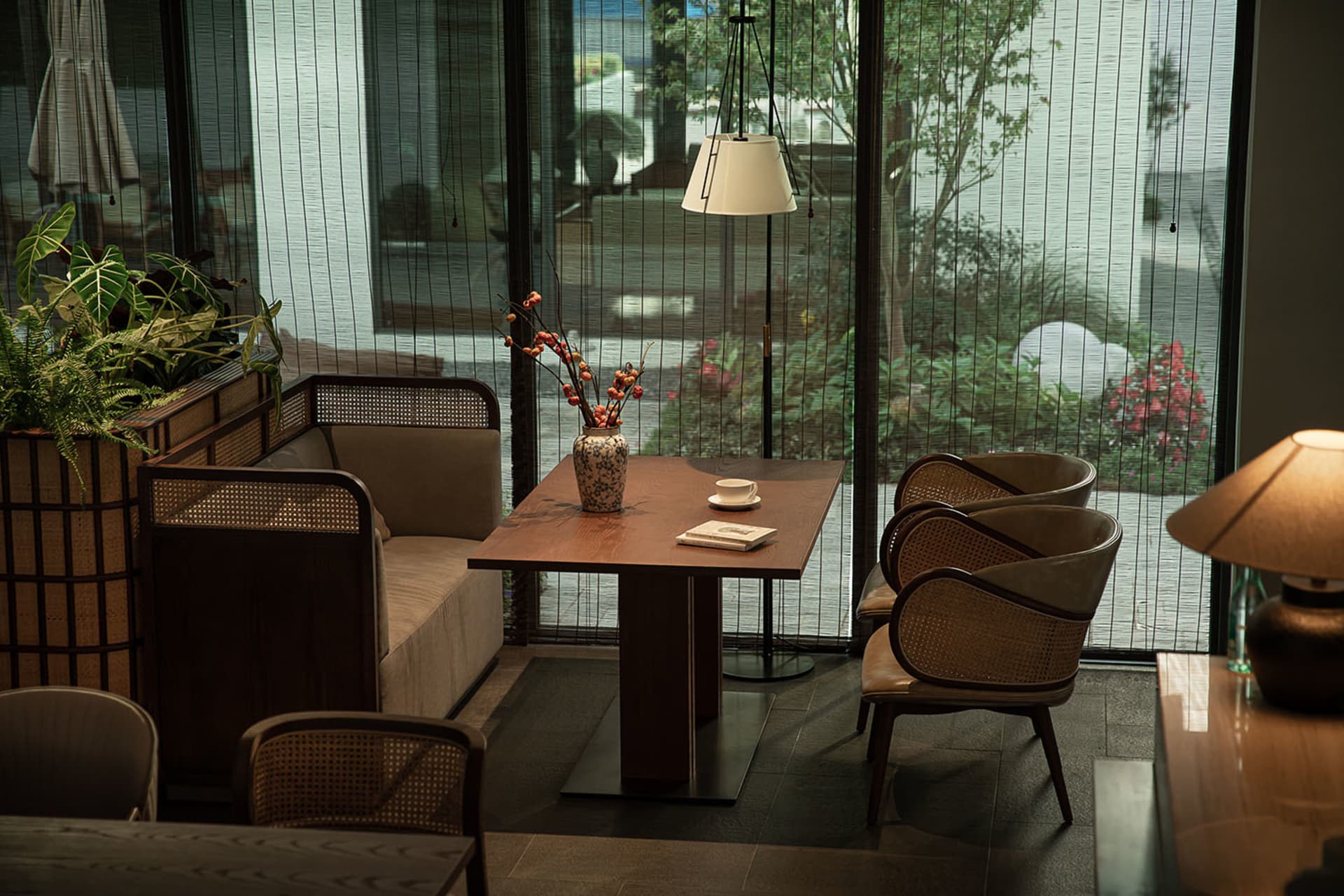 Modern living room with wooden furniture and potted plants, featuring a wooden table with a vase of flowers and a book, and r