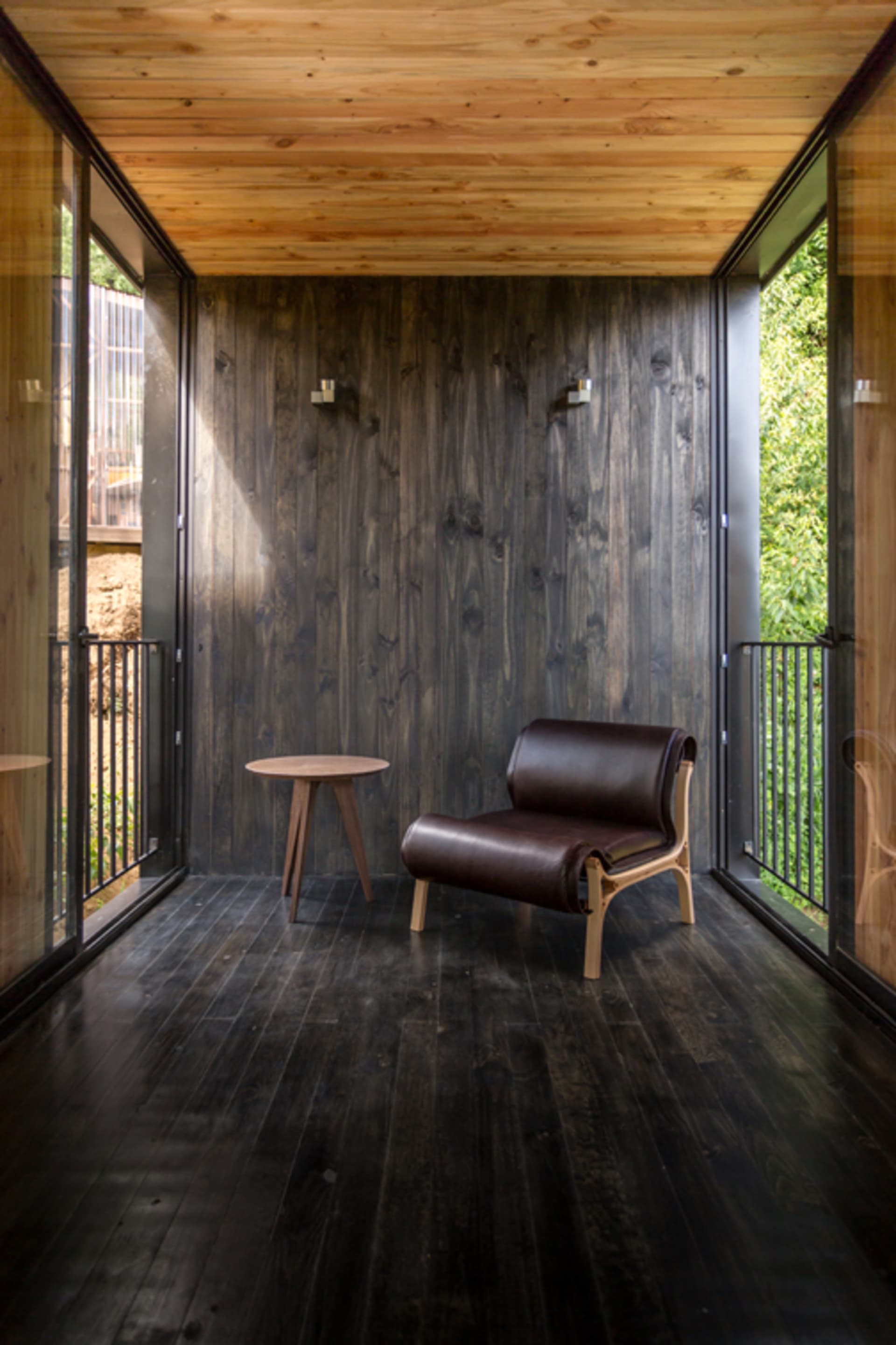 A cozy living space with dark wood walls, floor, and furniture, featuring a modern chair and small side table.