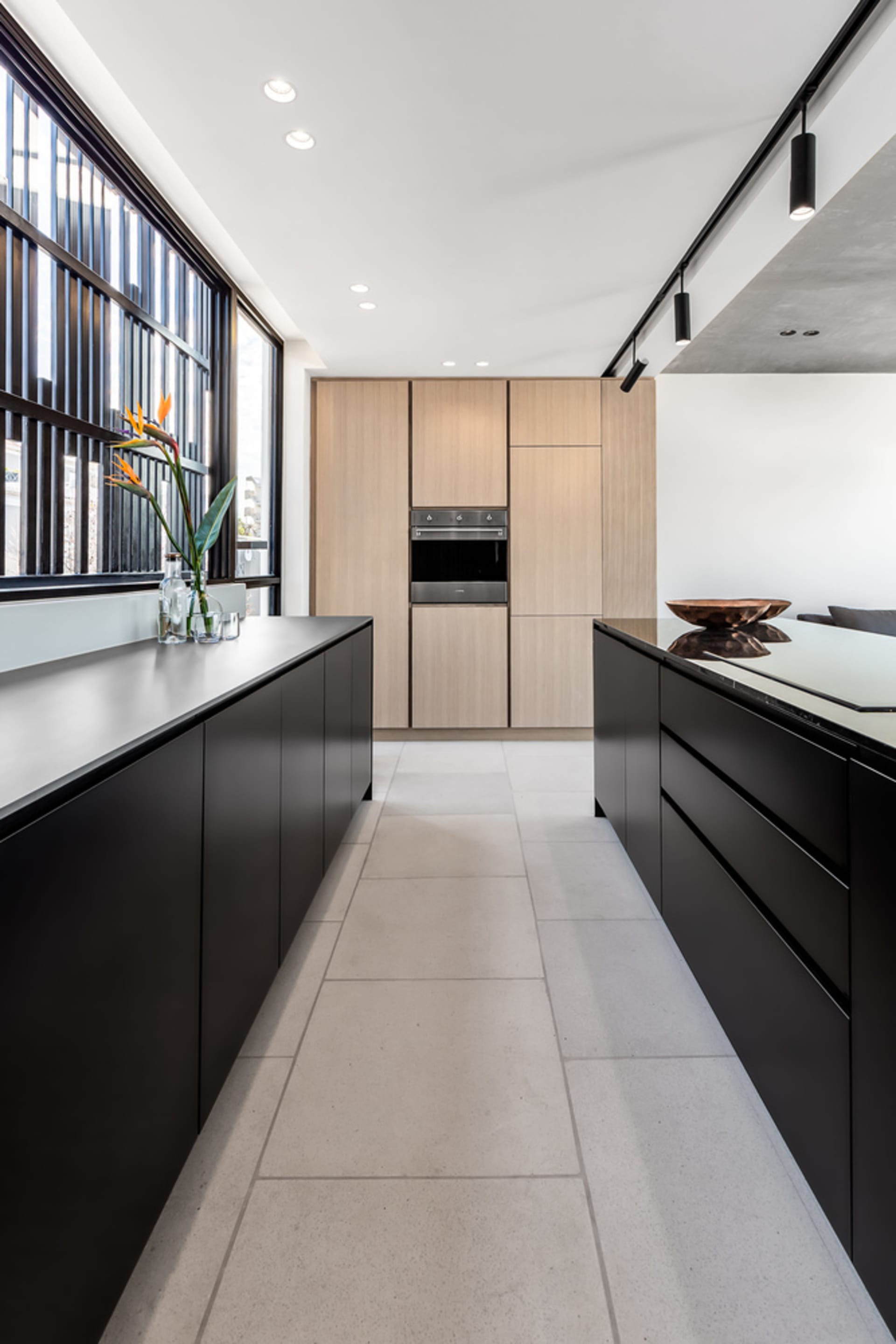 Modern, minimalist kitchen with wooden cabinets, black countertops, and floor-to-ceiling windows.
