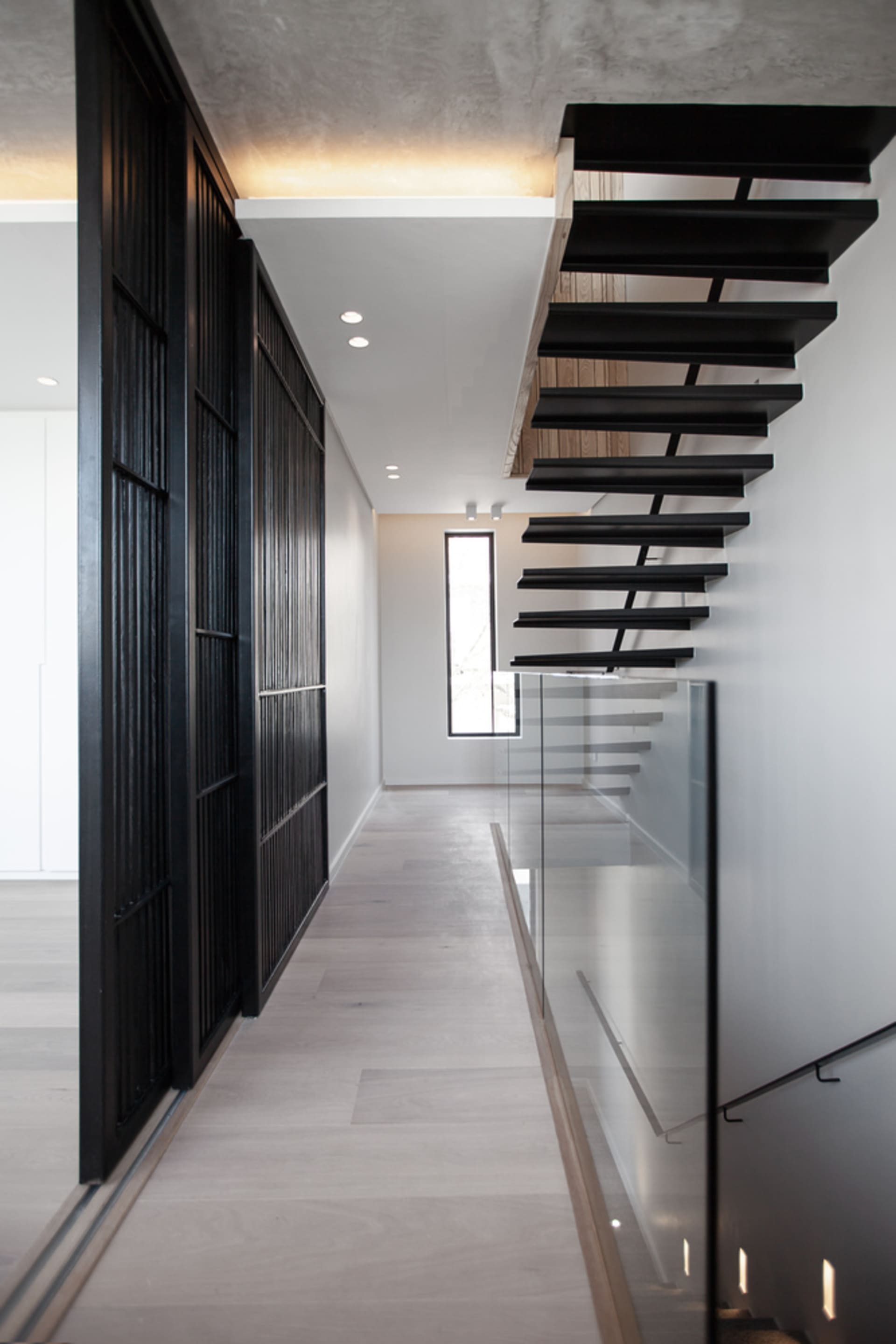 Modern minimalist house featuring a black staircase with glass railings and wooden floors.