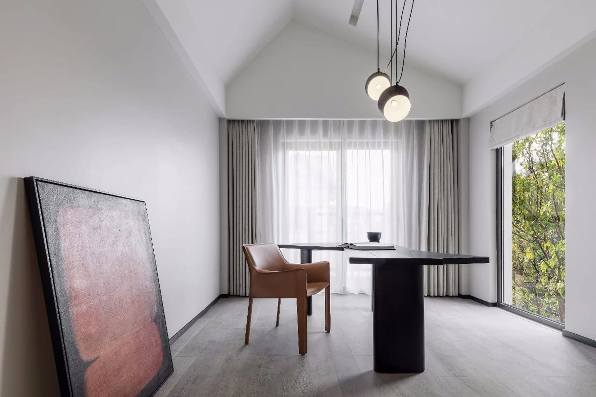 A minimalist study room featuring a black table, brown leather chair, large abstract painting, and white curtains