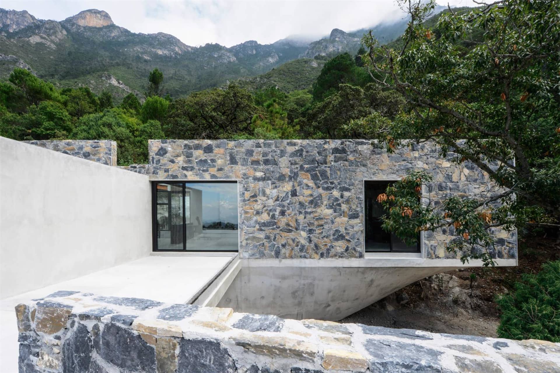 Modern exterior of a mountain residence featuring stone and concrete materials.