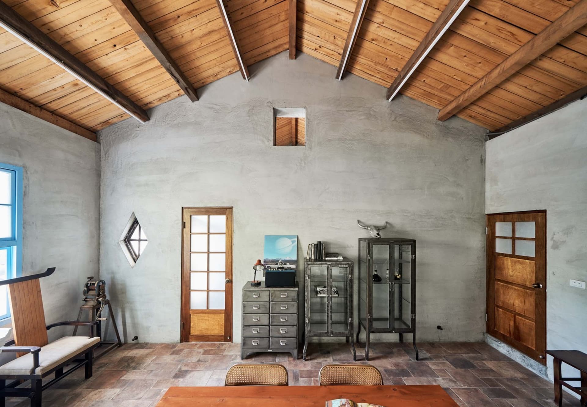 A modern, industrial-style living room with concrete walls, wooden furniture, and a high wooden ceiling with visible beams.