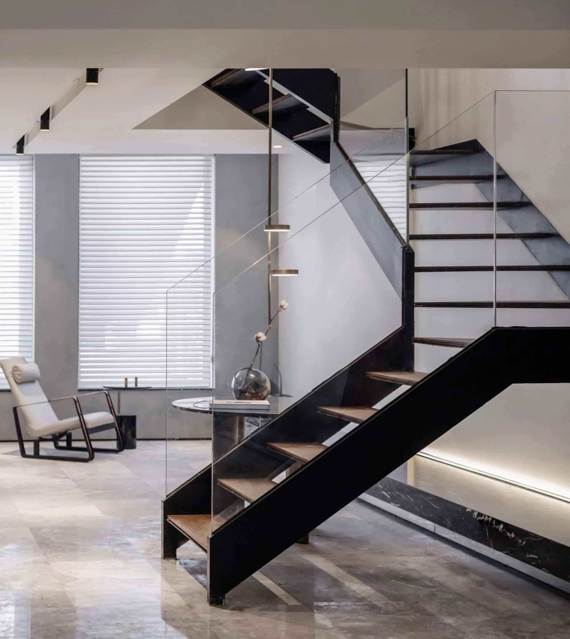 Industrial-style living room featuring modern metal staircase, glass wall, and marble flooring