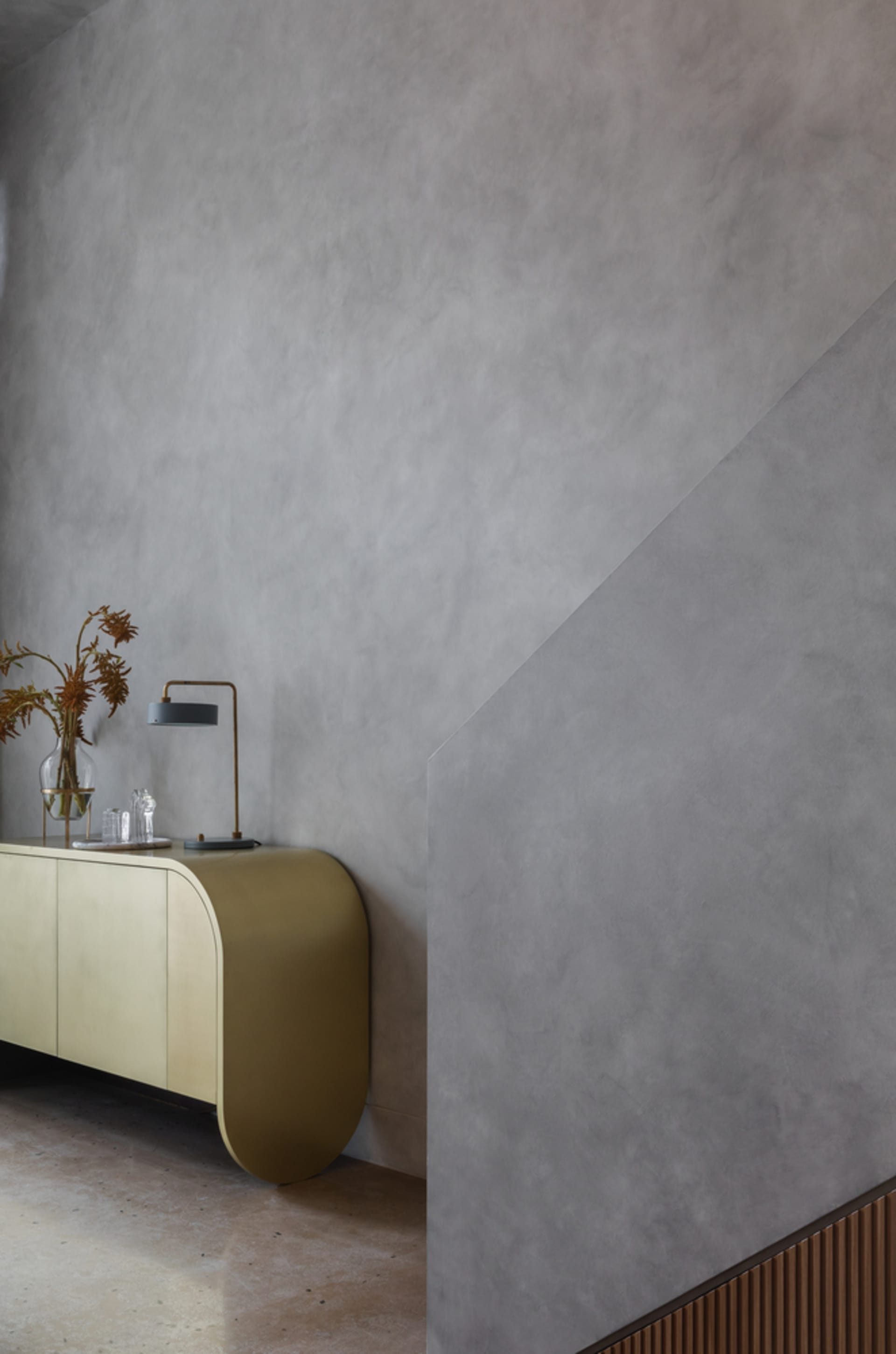A sleek, metallic console table with a smoked glass lamp and dried flowers in a vase.
