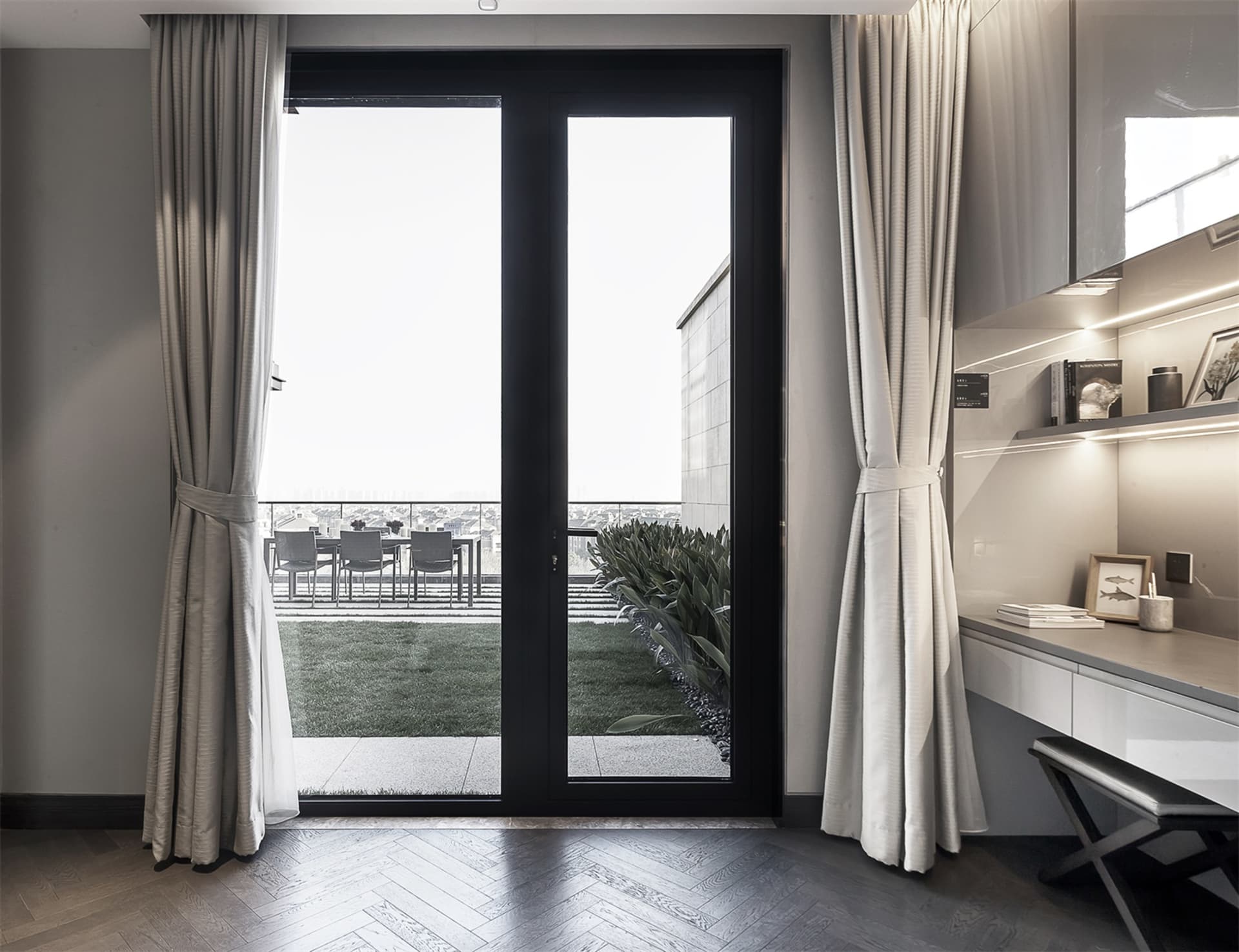 Modern, minimalist balcony with glass doors and white curtains, featuring a wooden floor and a view of a green outdoor area.