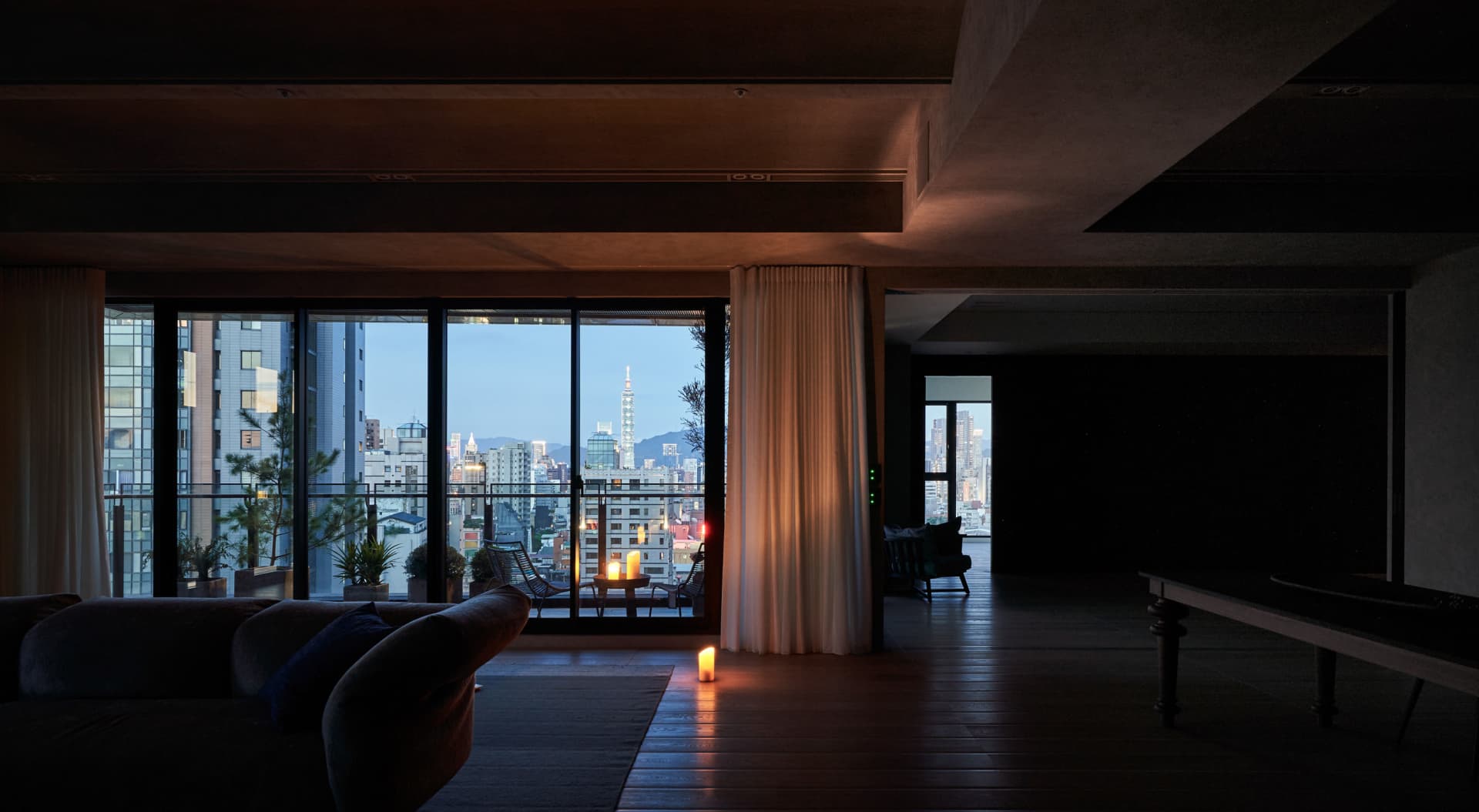 Modern living room with large glass windows overlooking a cityscape at dusk.