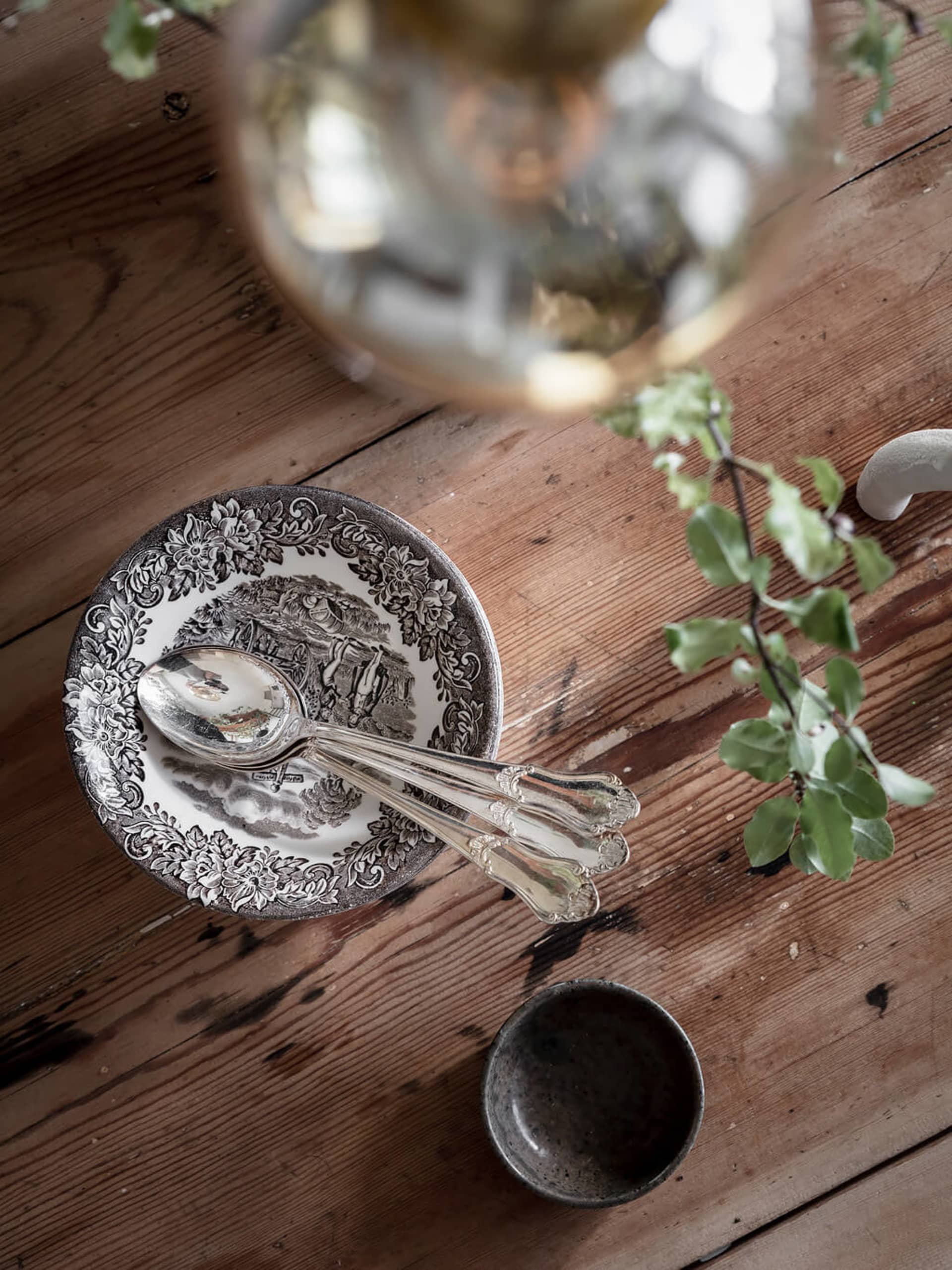 Table setting featuring a ceramic plate with intricate designs, a wooden bowl, and a glass vase with greenery.