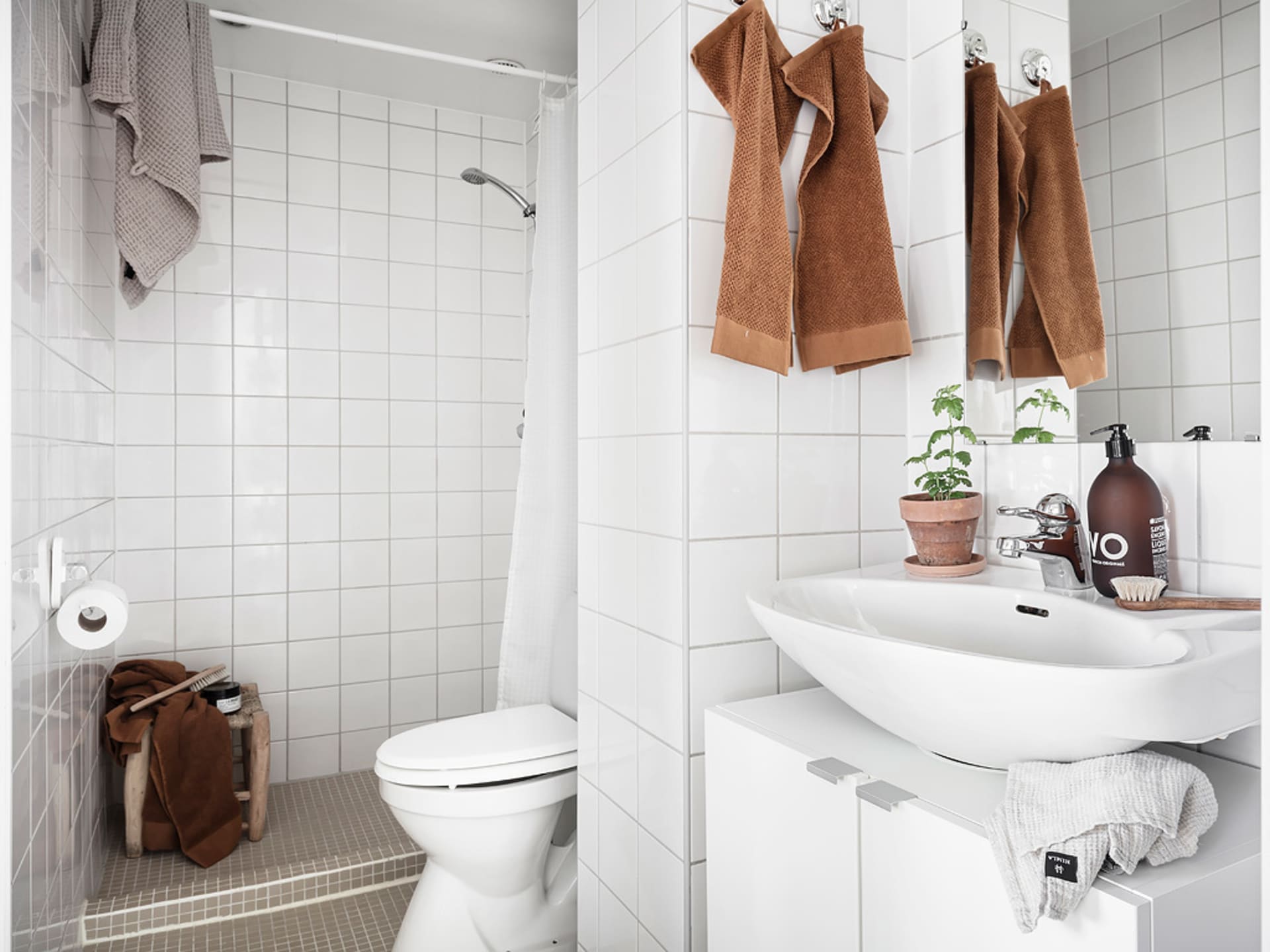 A minimalist bathroom with white ceramic tiles, a white toilet, a white sink, and brown towels hanging on the wall.