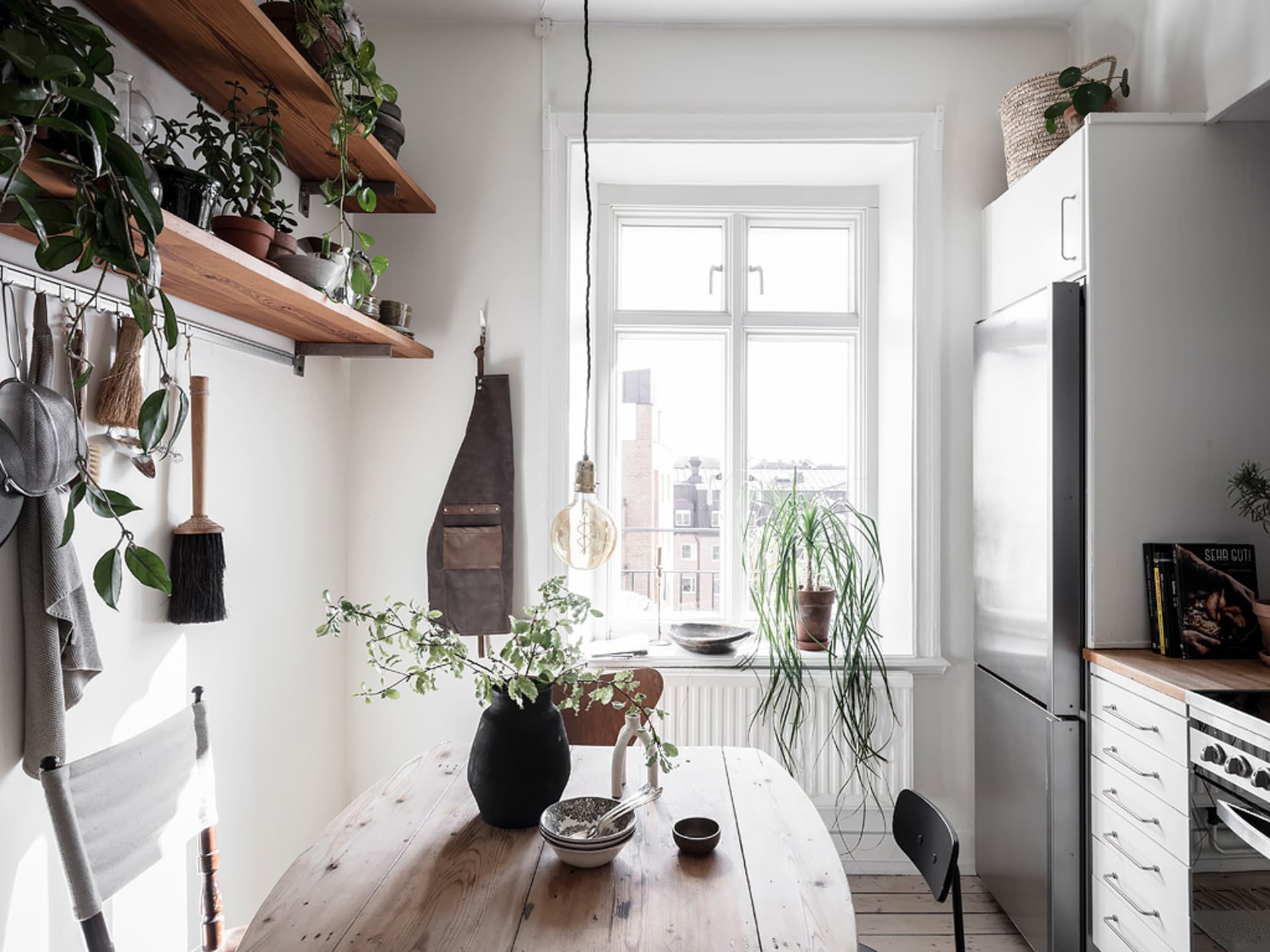 A minimalist kitchen featuring a wooden countertop, metal sink, and glass vase with greenery.