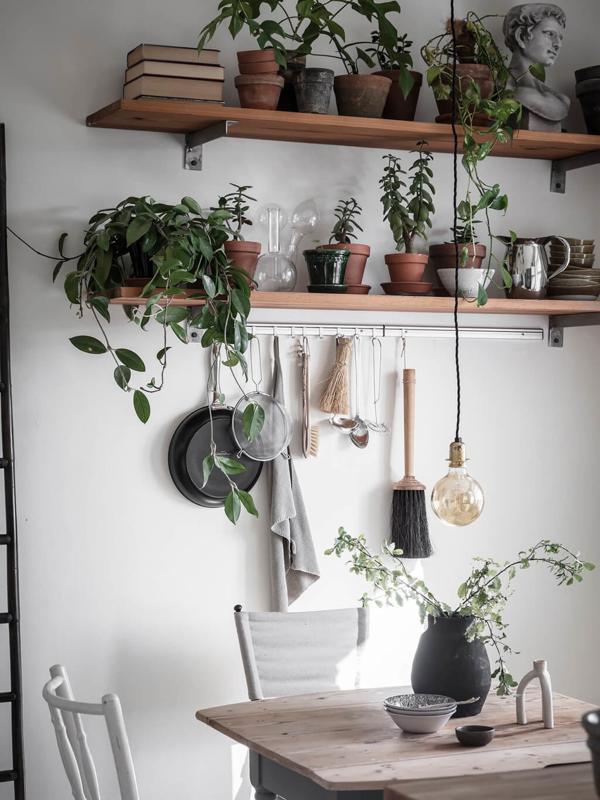 A minimalist kitchen wall adorned with reclaimed wood shelves, terracotta flower pots, and rustic hanging utensils.