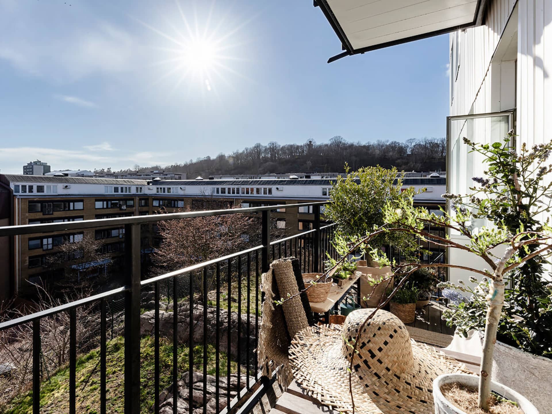 Modern balcony with steel railing, wooden furniture, and potted plants.