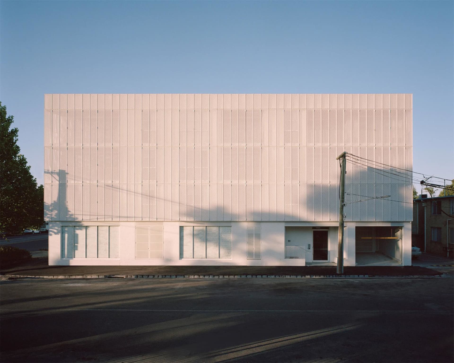 A modern building facade with white perforated panels and minimal windows.