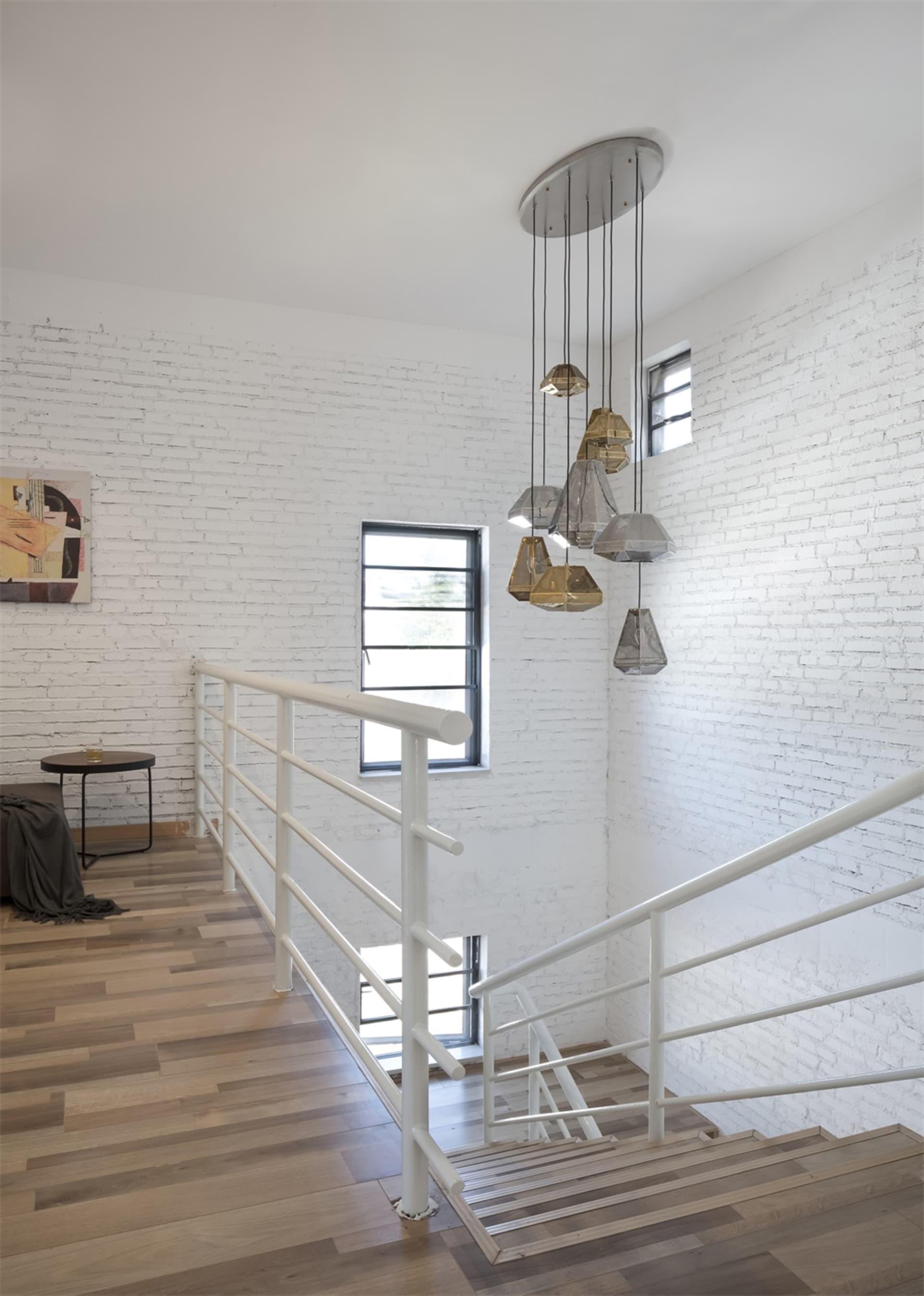 Modern interior staircase featuring brass lamps, white brick walls, and hardwood flooring.