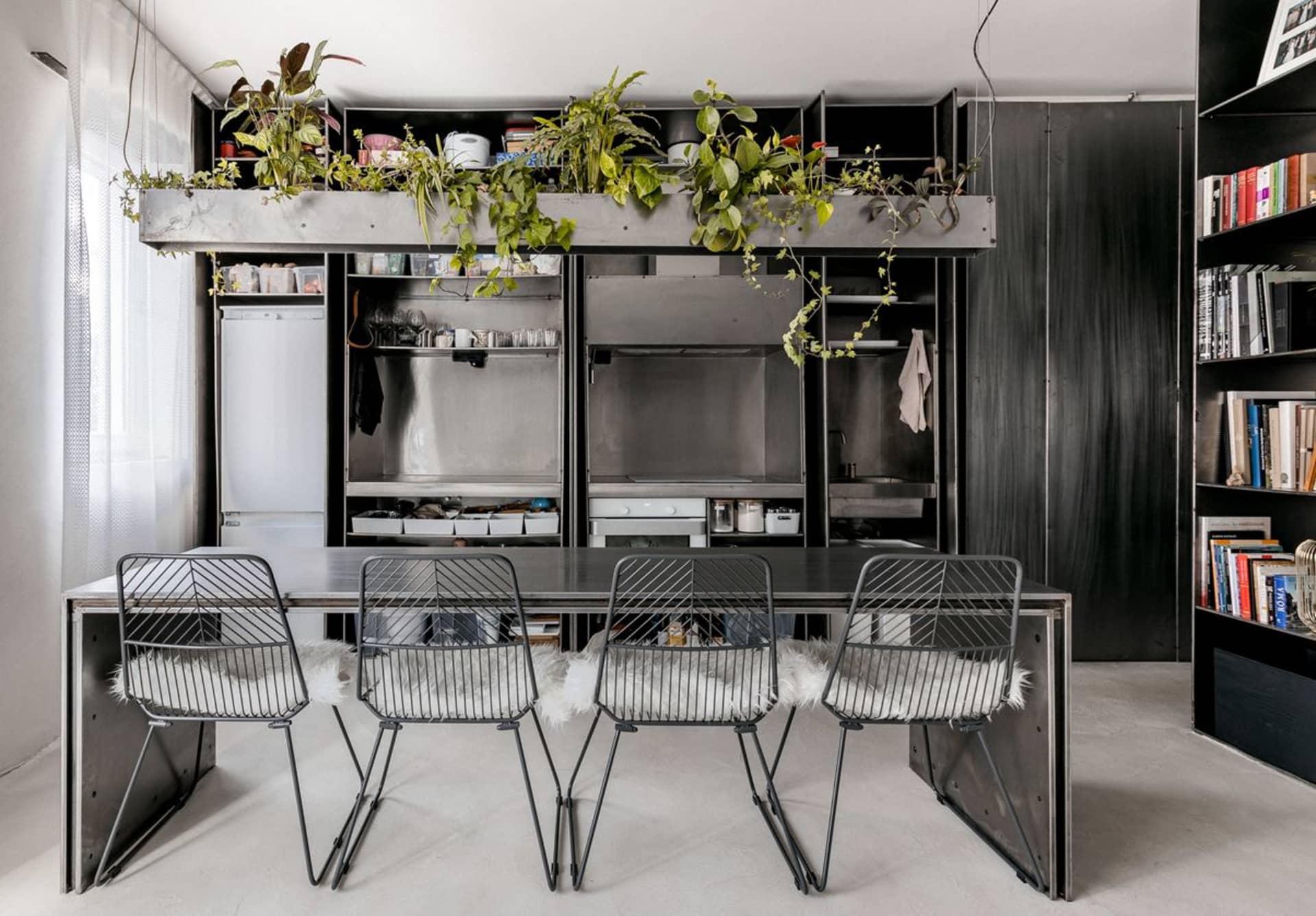 Modern urban housing unit with metal finishes, featuring a dining area with black metal chairs and table, and a kitchenette w