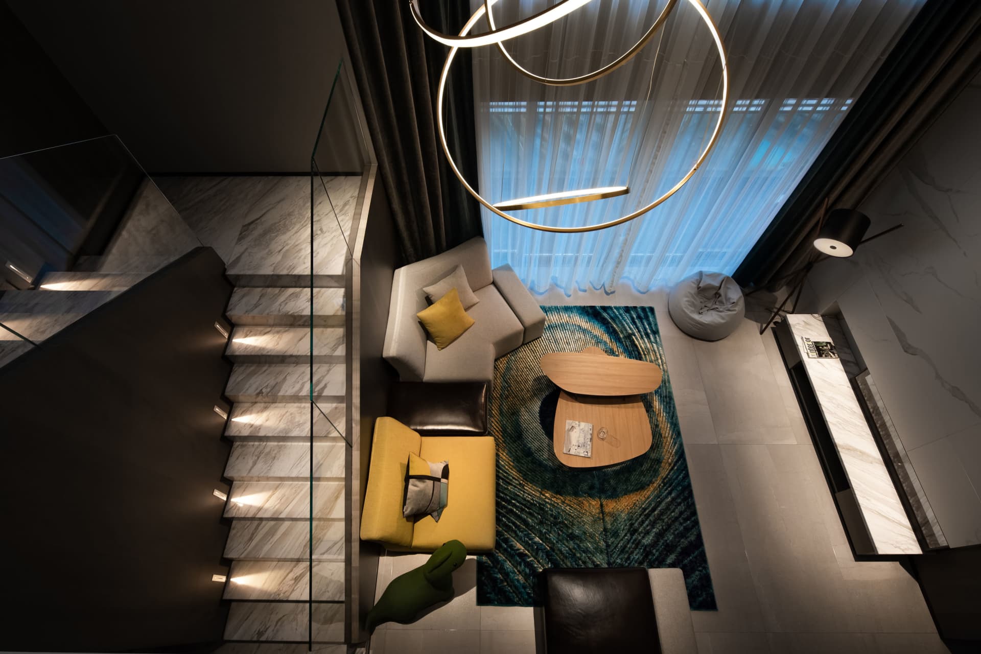 Top-down view of a modern industrial living room with marble stairs, glass chandelier, and leather furniture.