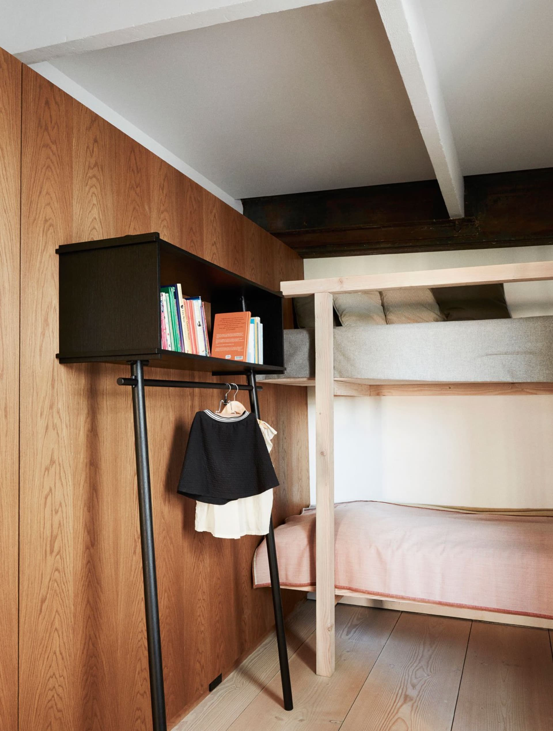 A minimalist bedroom with wooden walls and furniture, featuring a bunk bed and a black freestanding wardrobe.