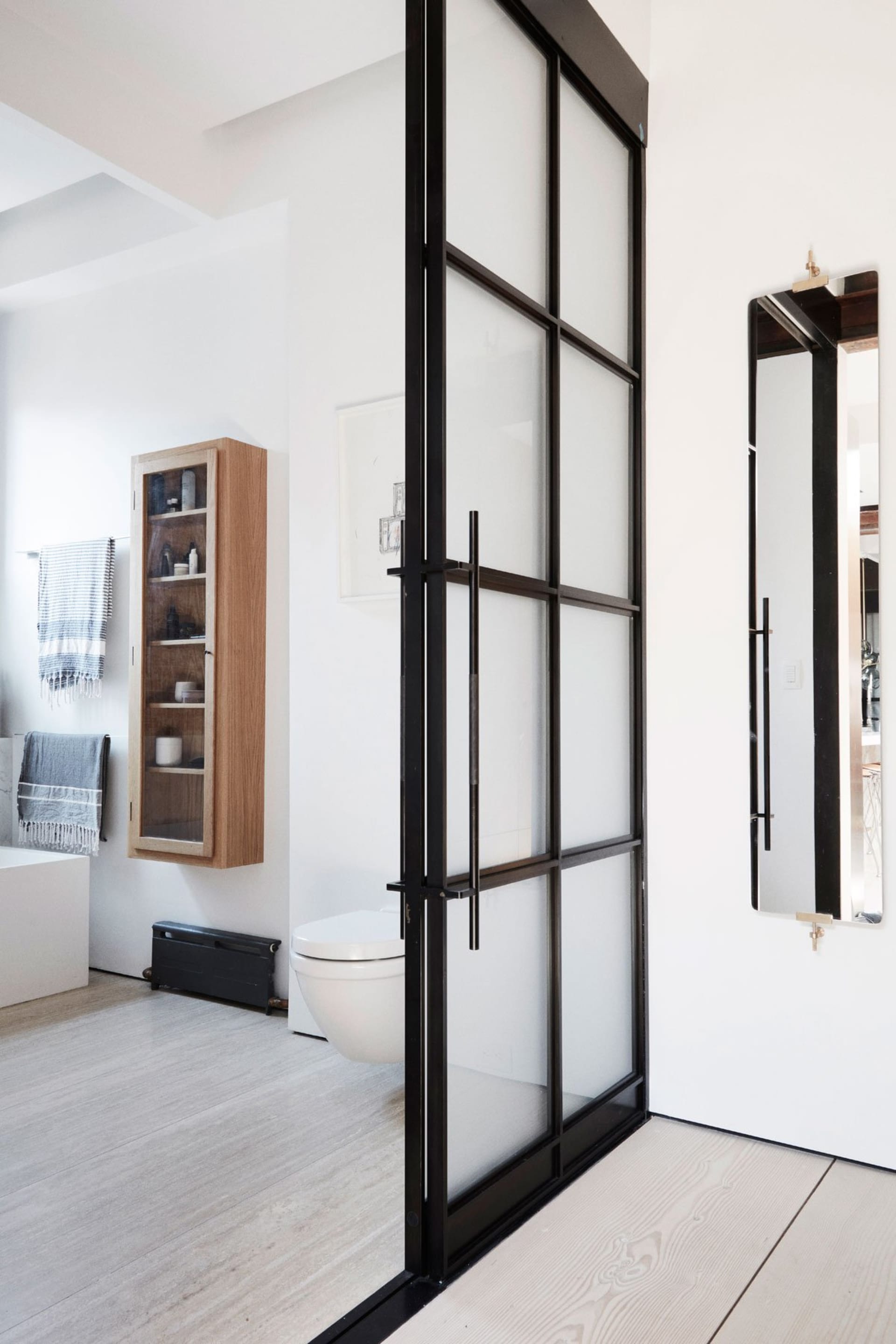 A modern bathroom with white furniture and a frosted glass door.