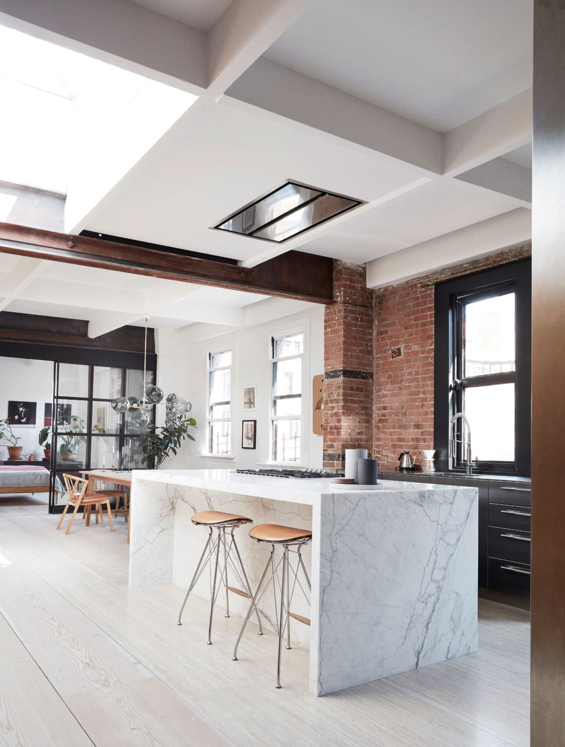 A modern kitchen featuring a white marble island, glass pendant lights, and an exposed brick wall.