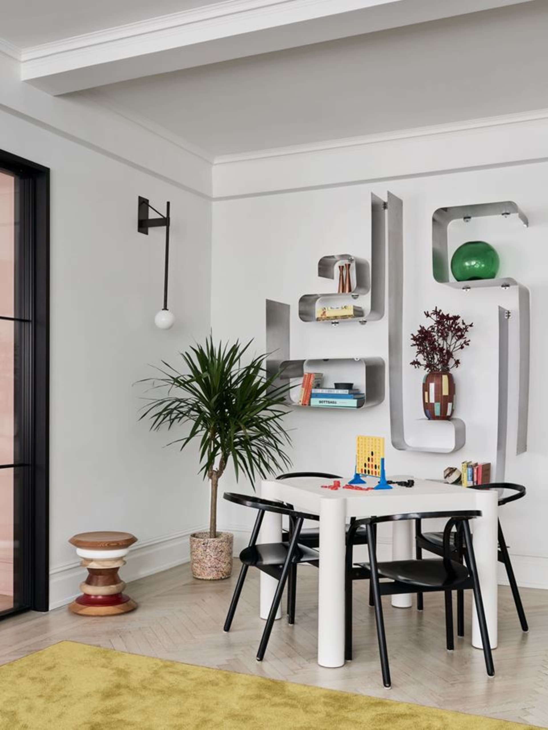 A minimalist living room with metallic floating shelves, a white table, and black chairs.