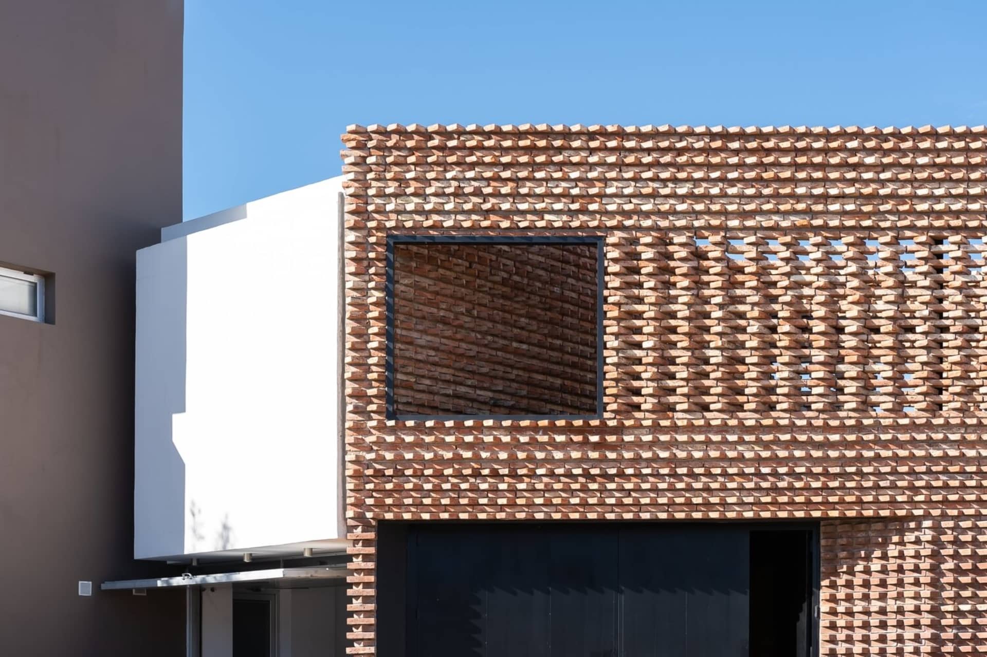 A modern building exterior featuring a brick facade with geometric patterns and a large window.