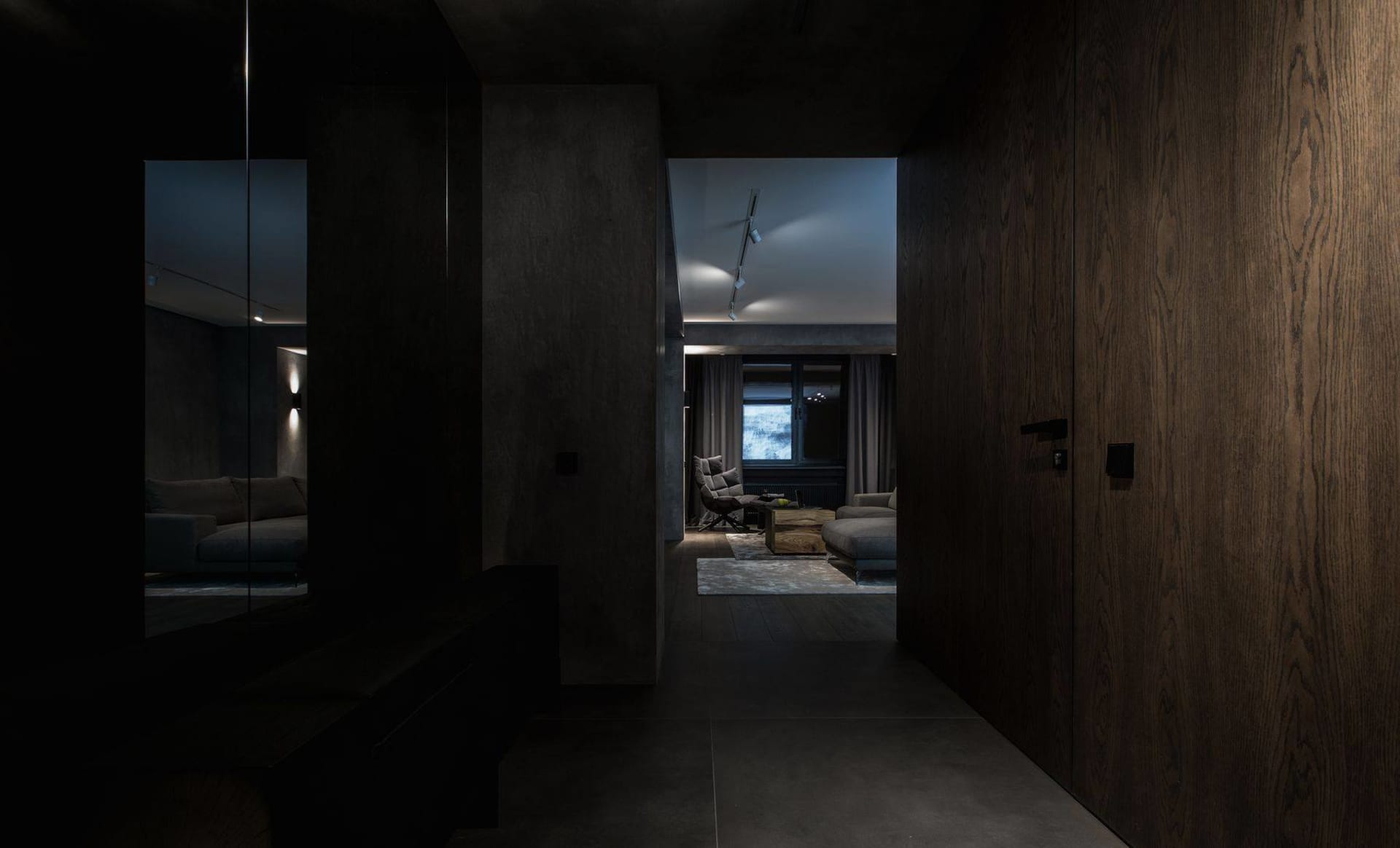 A spacious, modern living room with sleek, dark furnishings and concrete walls.