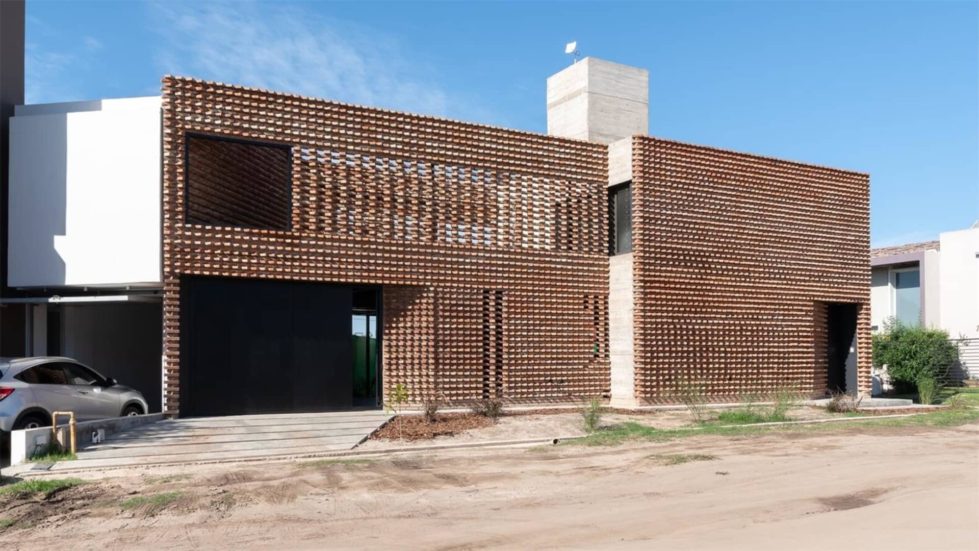 A modern house with a brick exterior featuring large windows and a concrete roof.