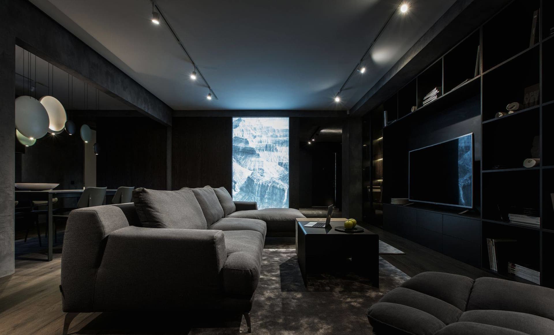 Industrial living room with concrete walls and floor, featuring a large sectional sofa, a coffee table with a laptop and an a