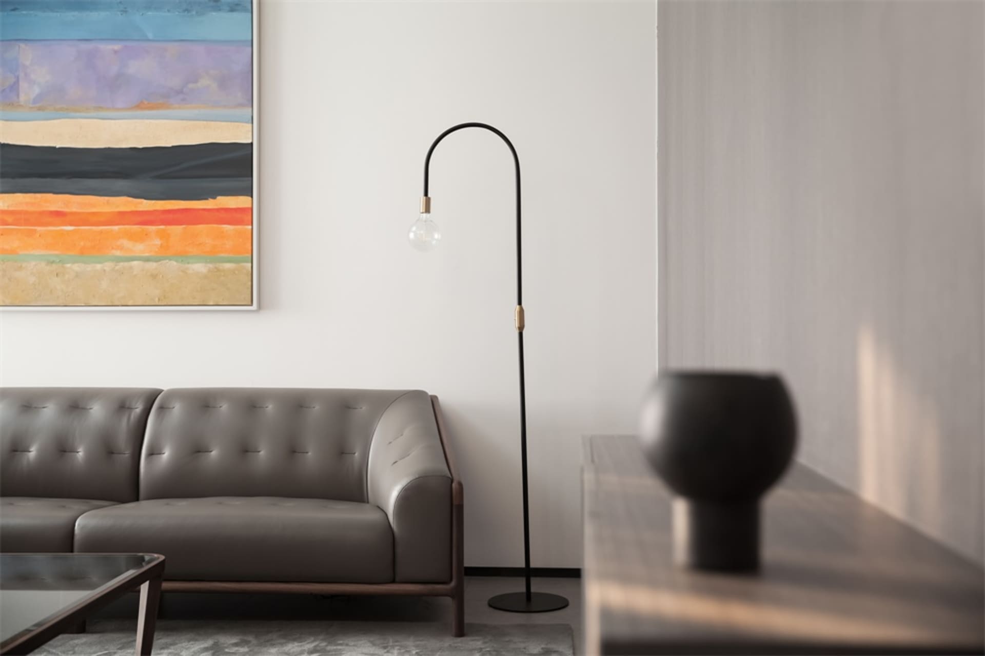 A modern living room with a black metal floor lamp, gray leather sofa, and colorful abstract art on the wall.